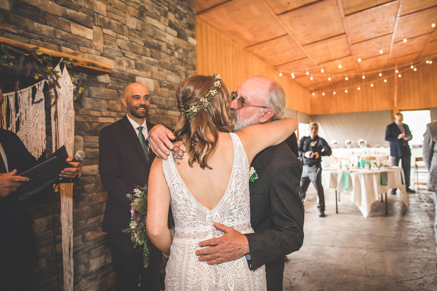 Indoor wedding ceremony with string lights and stone wall backdrop.