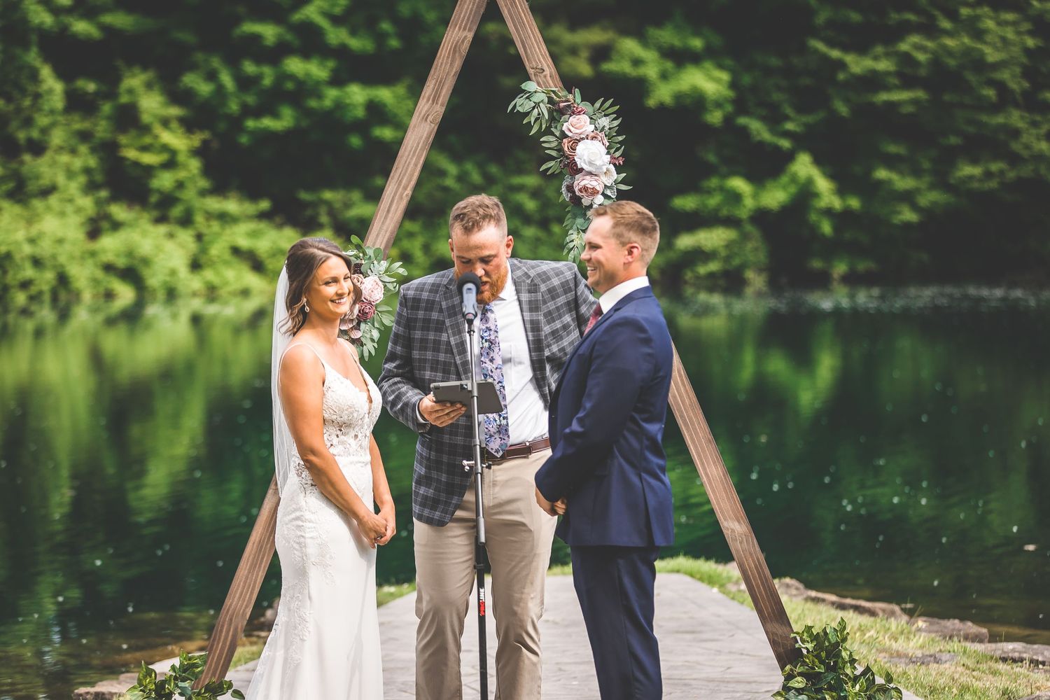 Intimate lakeside wedding ceremony with rustic wooden triangle arch and natural decor.