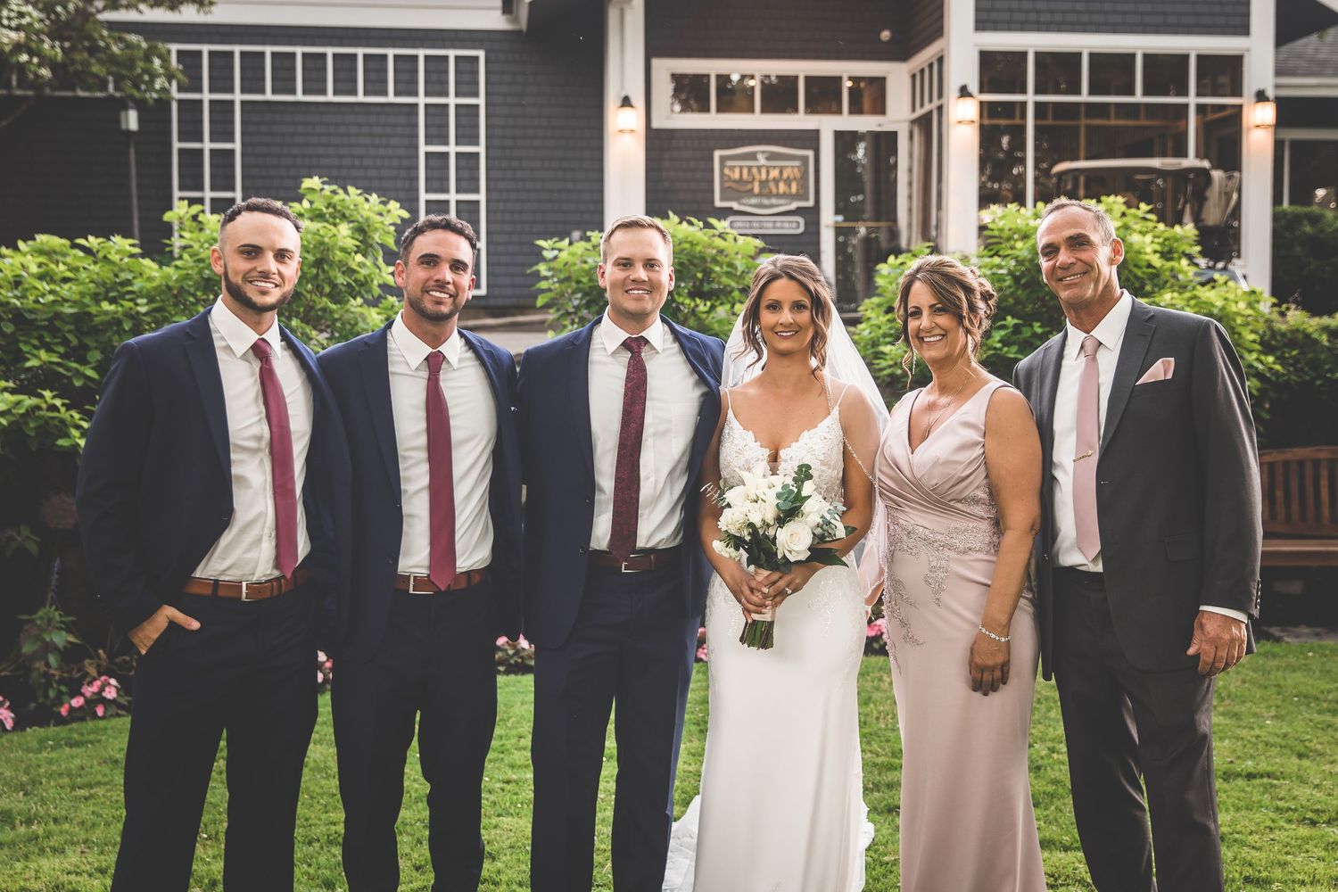 Wedding party poses outside dark gray building with white trim.