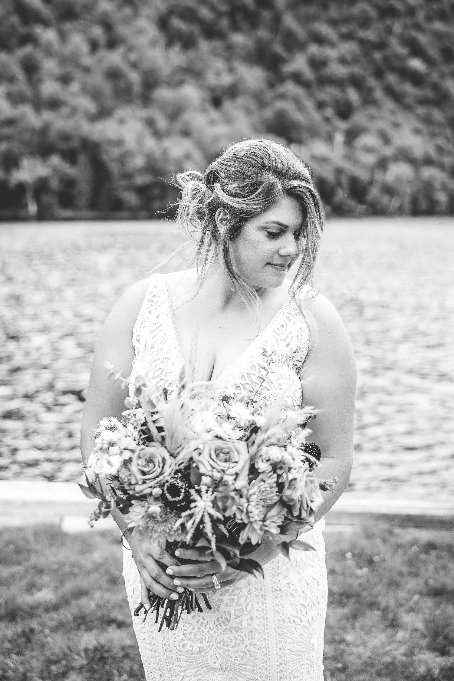 Black and white photo of bride holding beautiful wildflower bouquet against lake backdrop.