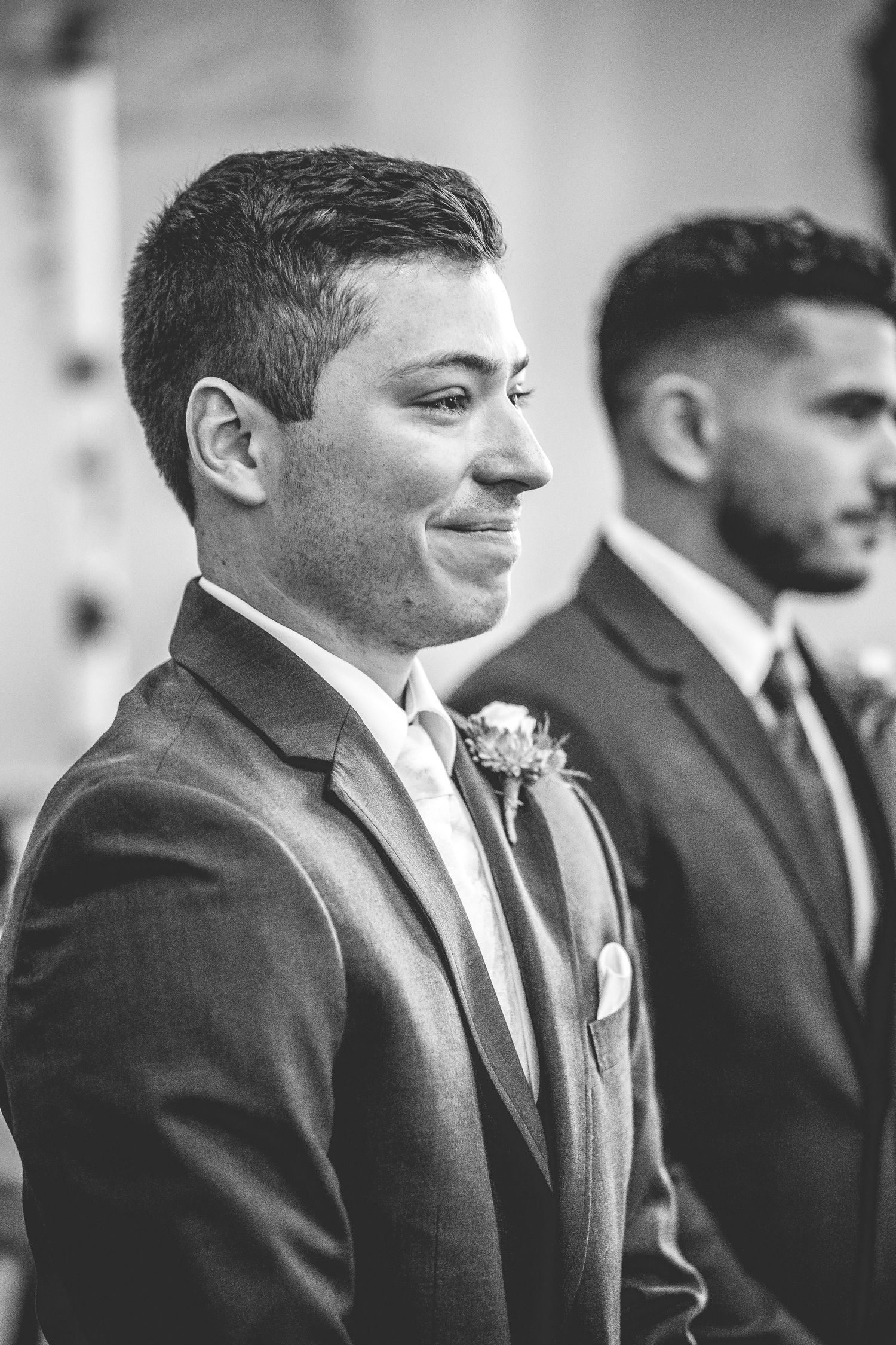 Row of groomsmen in black suits and ties lined up at a wedding ceremony.