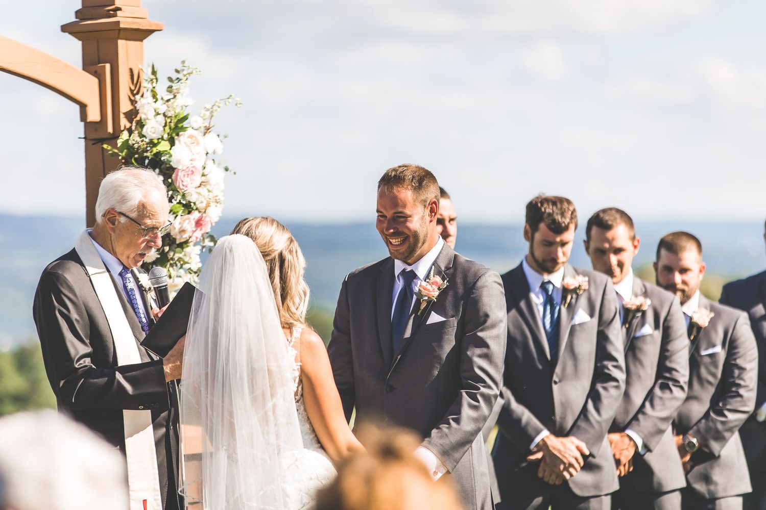 An outdoor wedding ceremony with decorative floral arrangements and groomsmen standing at attention.