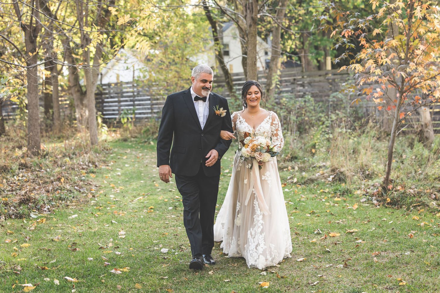 Wedding party walks along a wooded path during an autumn outdoor ceremony.