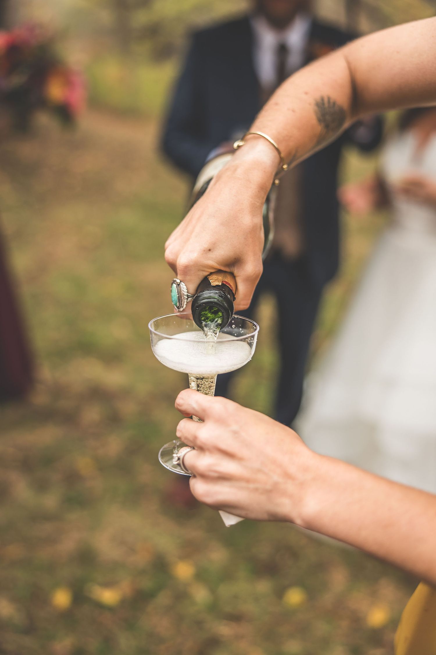 Close-up of hands pouring celebratory drinks at outdoor wedding reception.