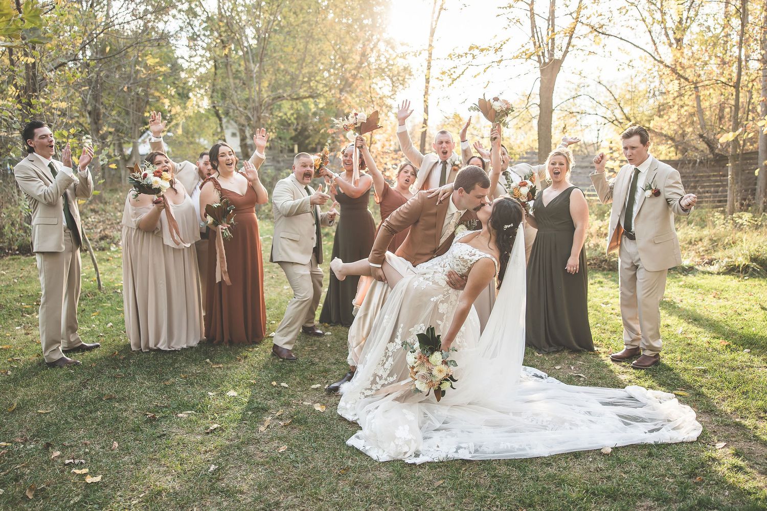 Wedding party poses together in an autumn forest setting with warm golden light filtering through the trees.