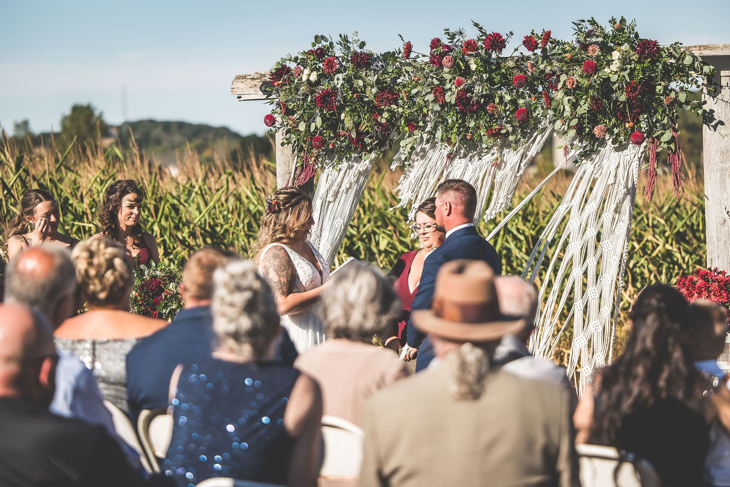 Wedding guests watching ceremony under floral arch with macrame decorations.