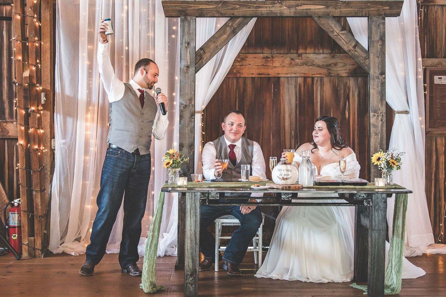 Rustic barn wedding venue decorated with flowing white curtains and warm lighting.