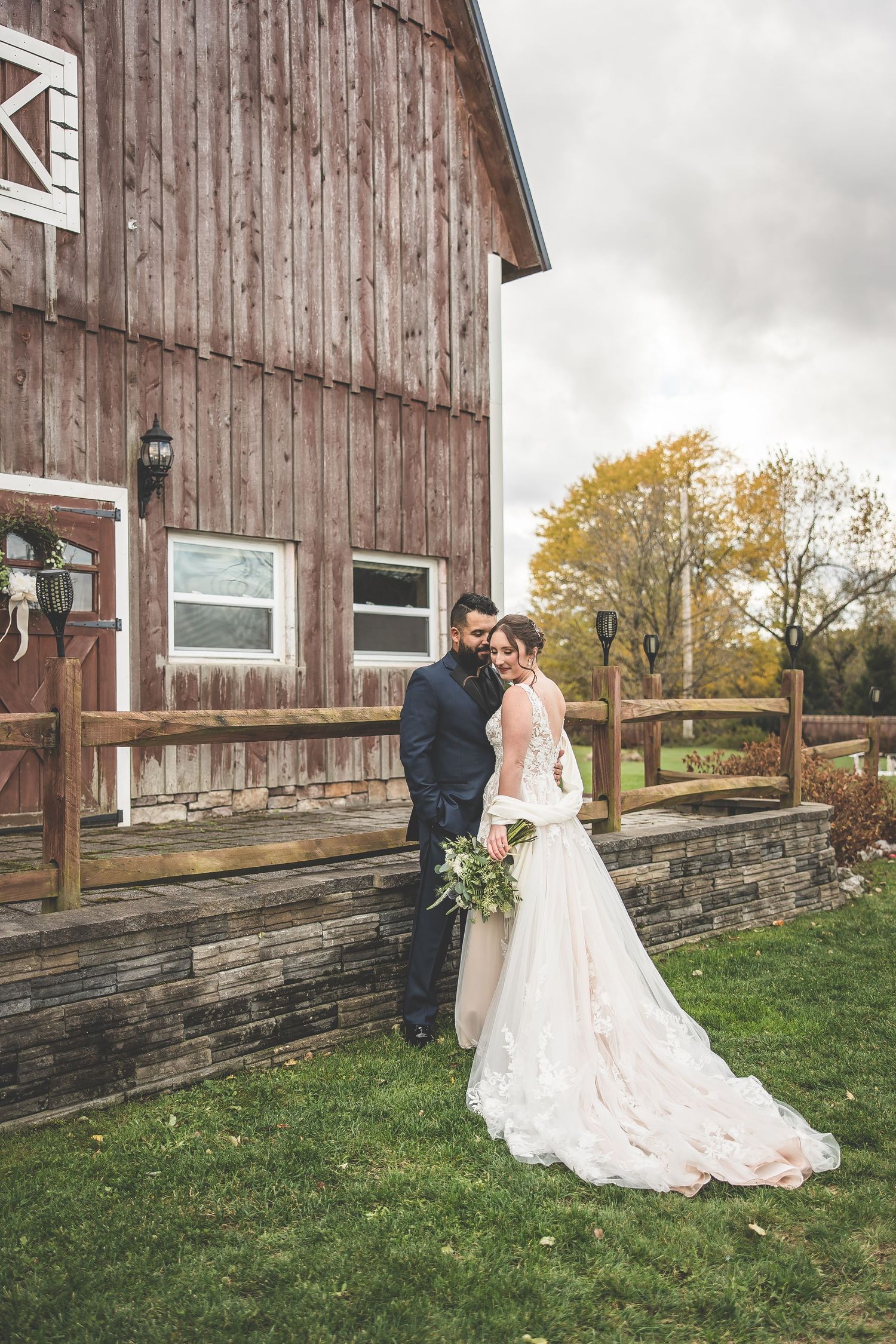 Rustic barn wedding portrait with long train dress against weathered wooden walls.