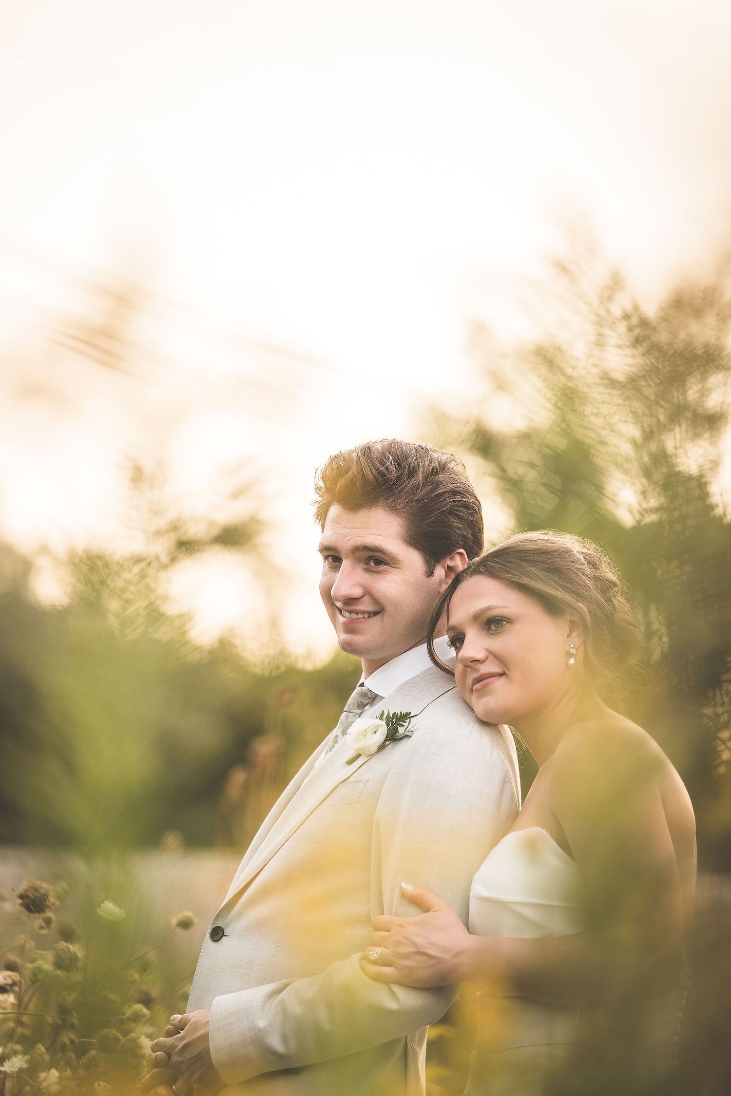 Couple shares tender moment in golden sunlit meadow during wedding photoshoot.