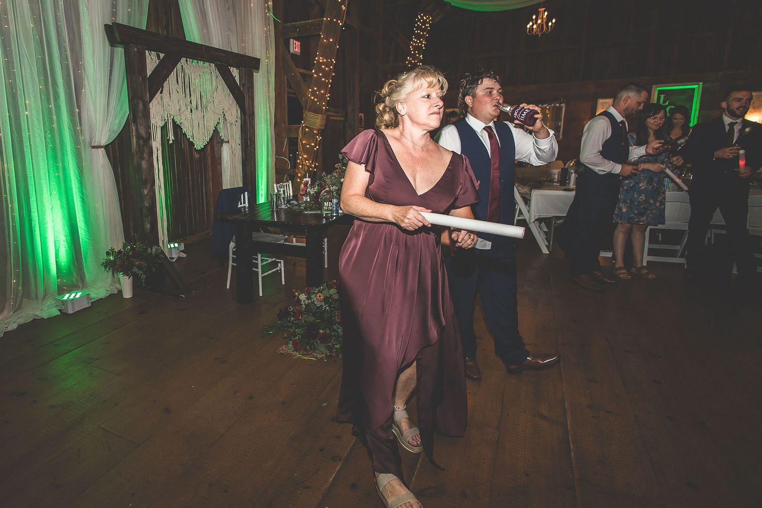 Wedding reception dance party in a barn with green accent lighting and wooden beams.