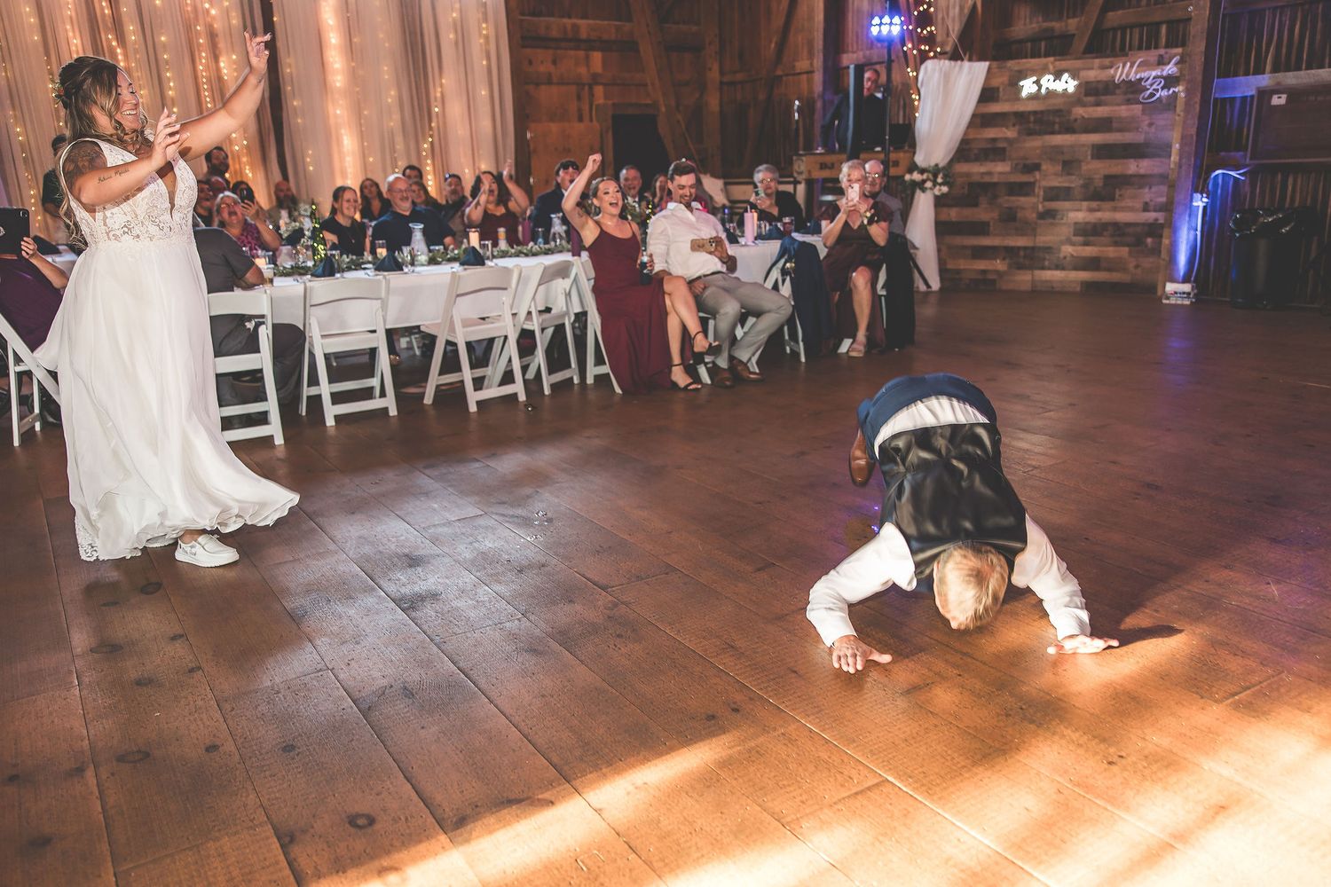 Dancers move gracefully across a rustic wooden barn floor during a wedding reception.