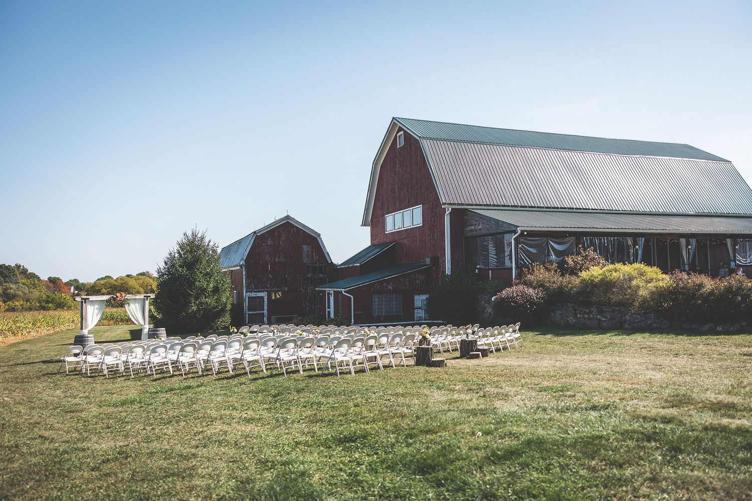 Panoramic view of a rustic farm wedding venue with red barn and ceremony setup.