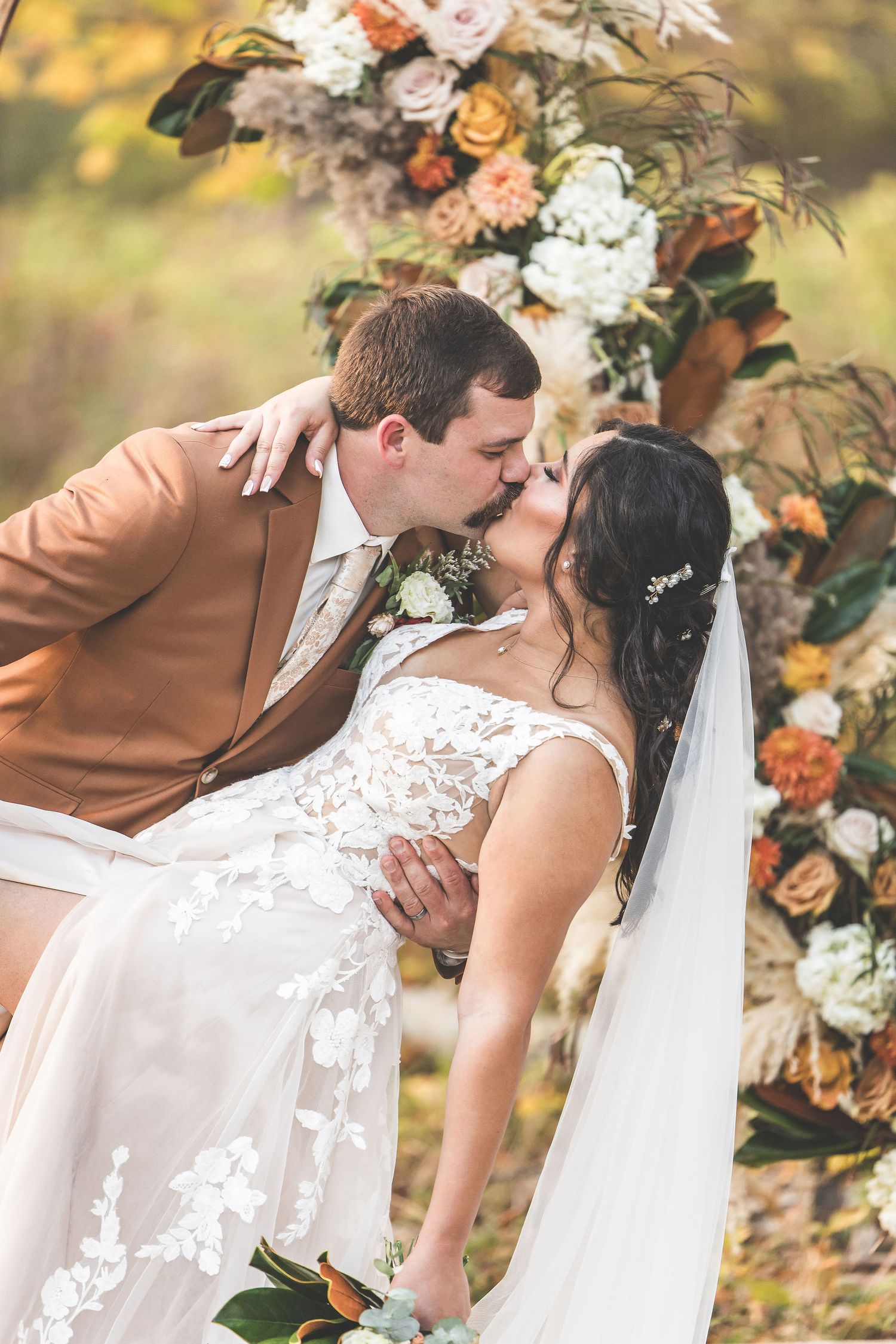 Romantic wedding moment captured in front of floral arrangements with warm autumn colors.
