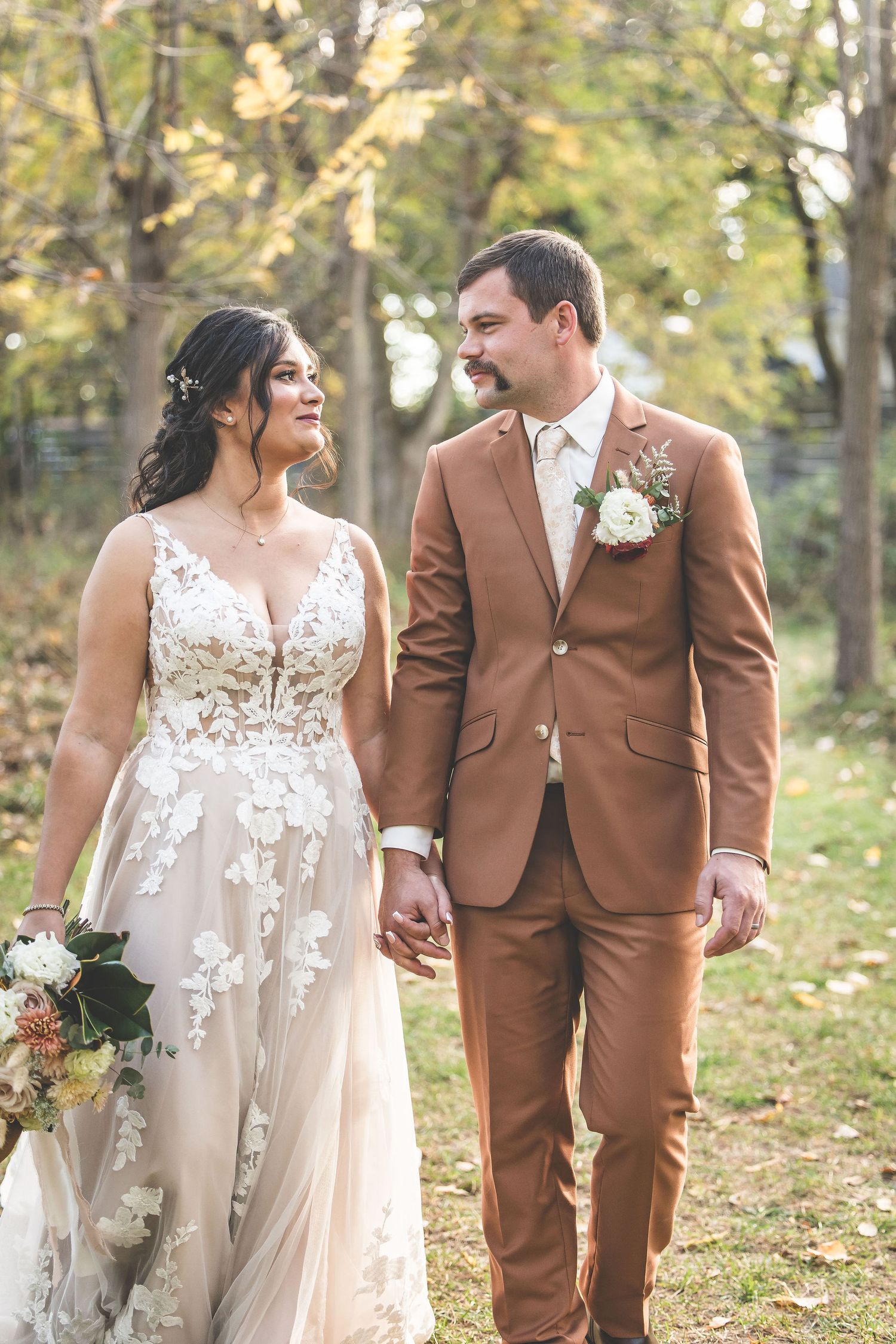 Newlyweds share tender moments while walking together in a sunlit forest setting.