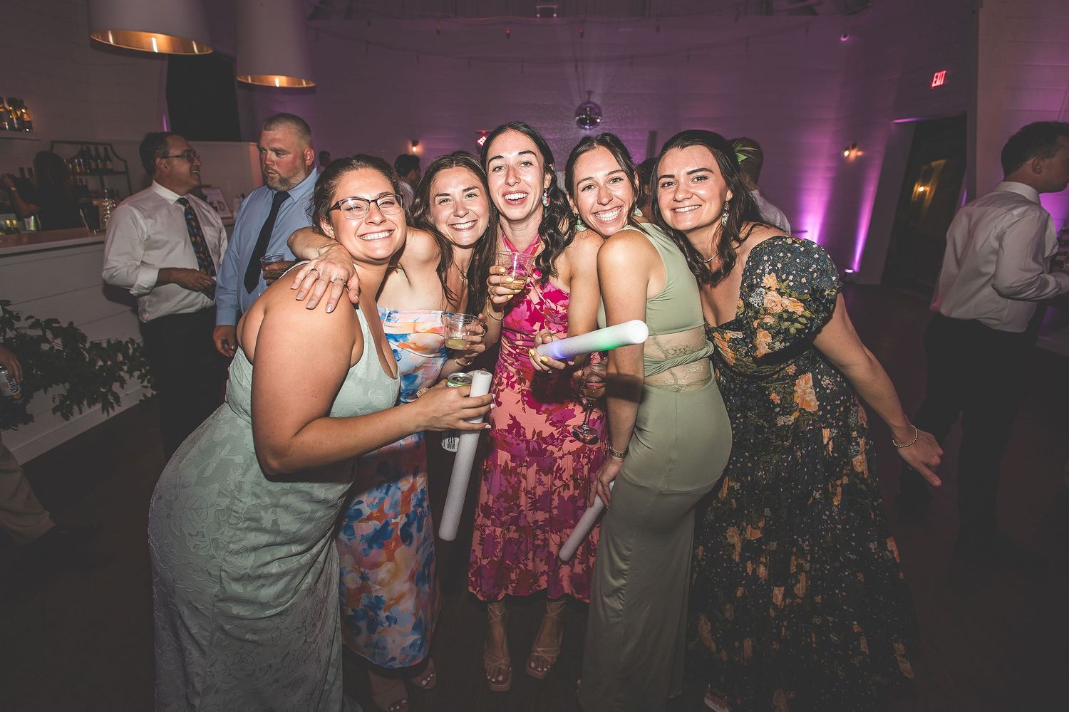Wedding party guests dancing and celebrating on a dimly lit dance floor with purple lighting.
