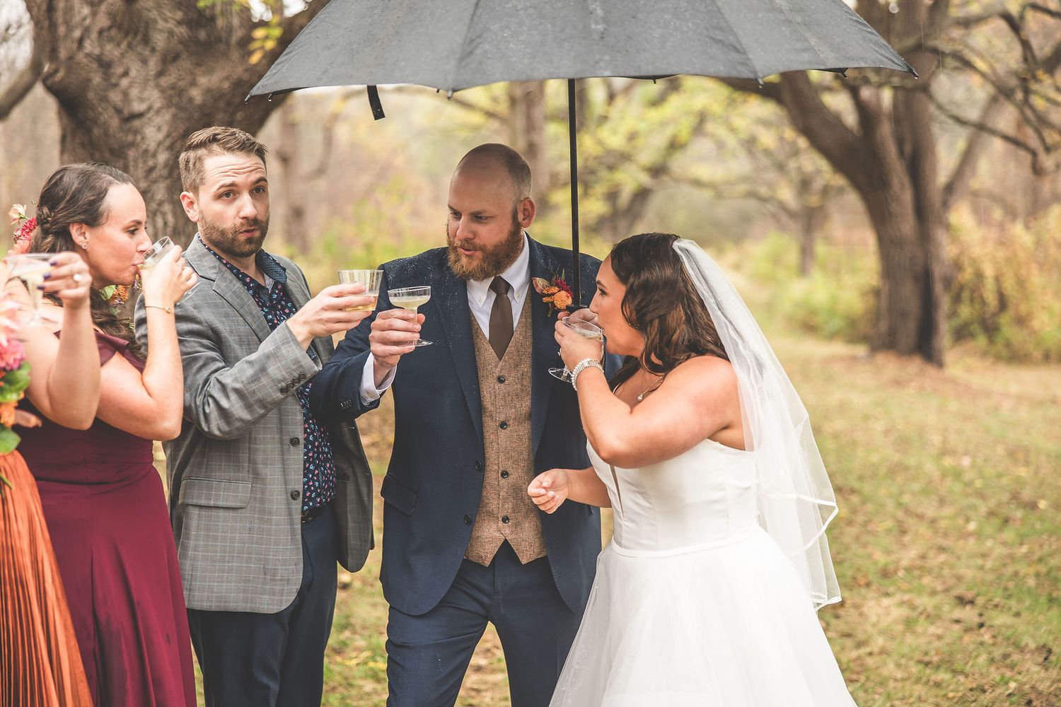 Wedding celebration beneath large black umbrella during fall outdoor ceremony.