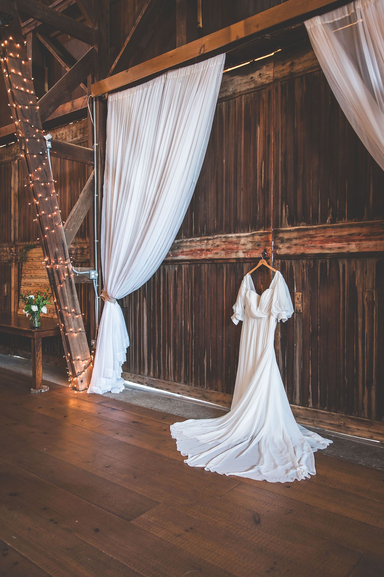 Rustic barn interior with white draping and string lights creating romantic ambiance.