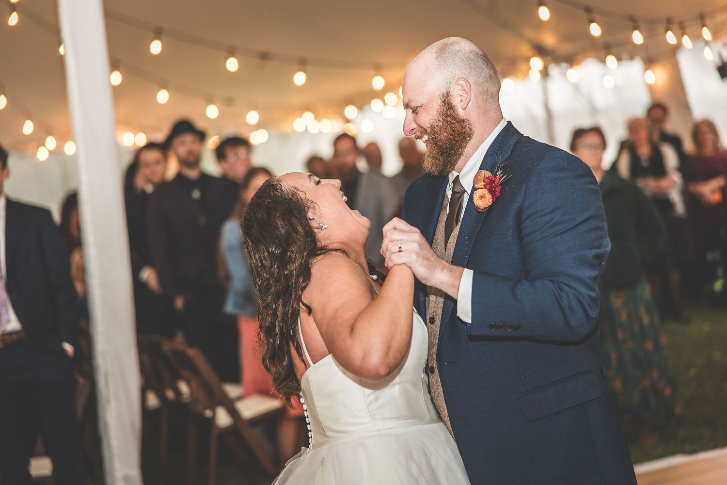 Wedding couple performs their first dance under warm string lights with guests looking on.