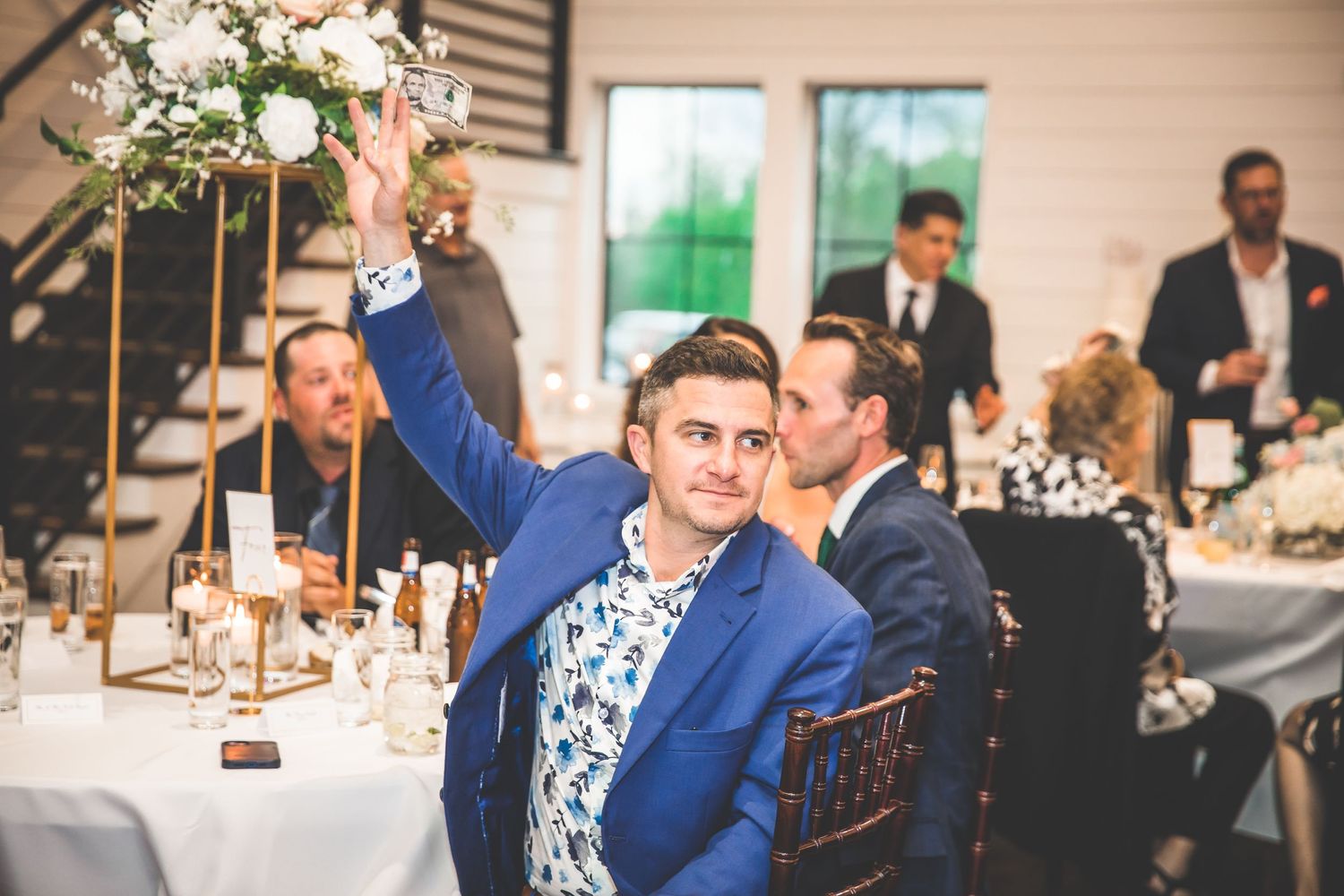 Wedding reception guests enjoying dinner and conversation at decorated tables in elegant venue.