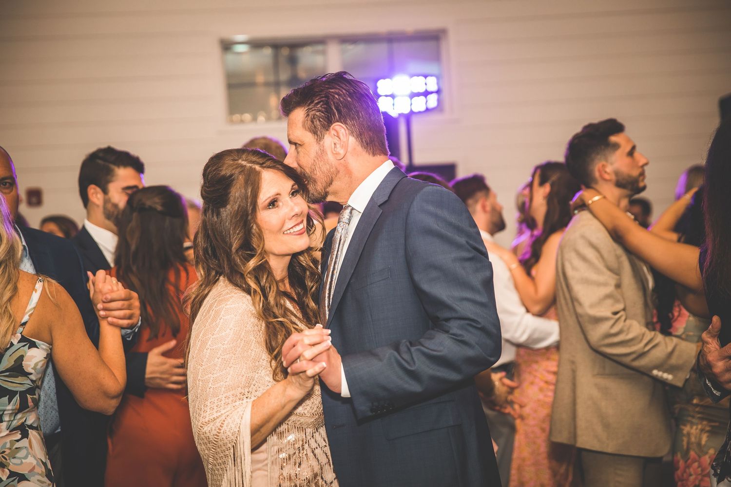 Couples dance together during an evening reception with ambient lighting and a festive atmosphere.