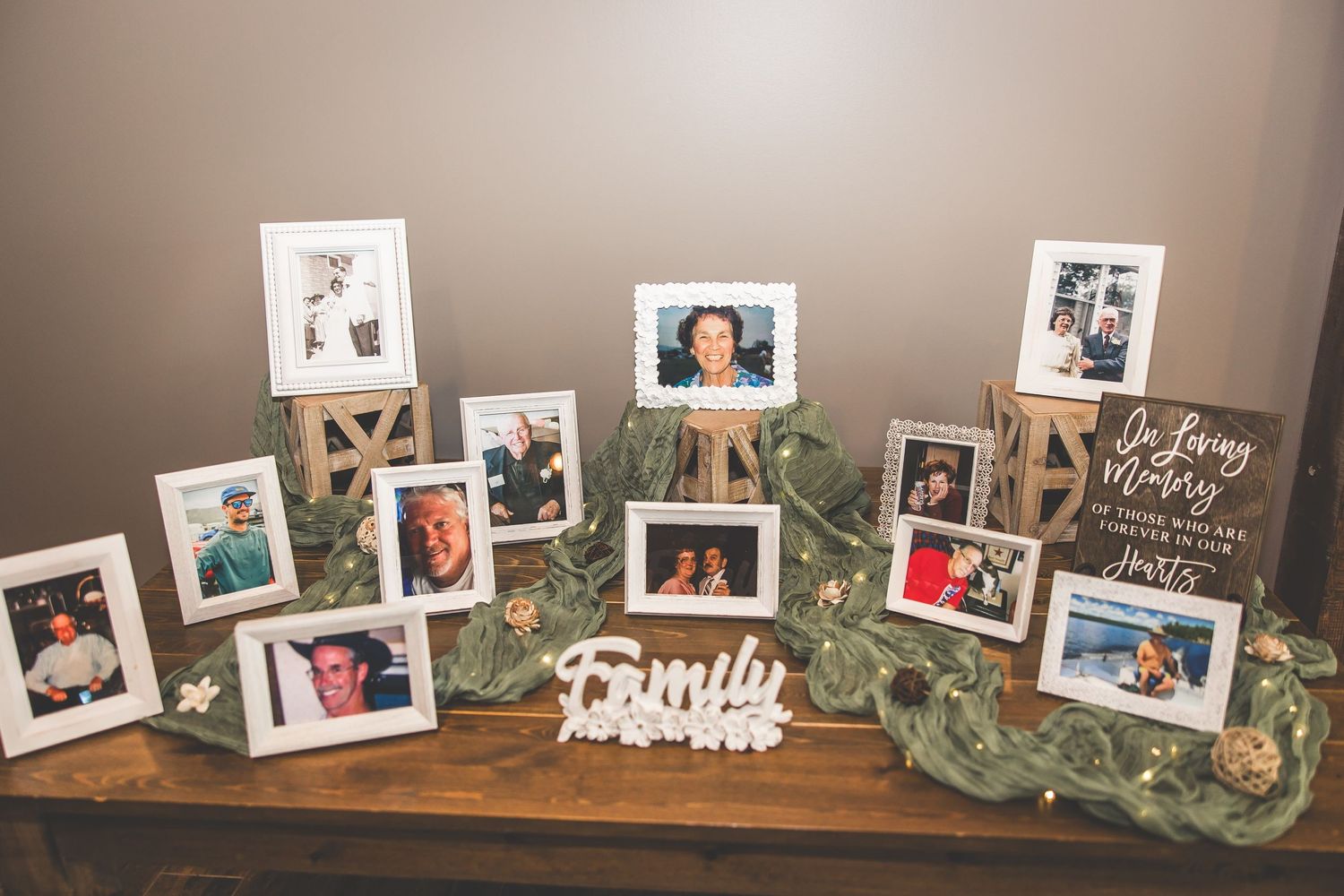 Wedding photo display on wooden shelf with greenery and family pictures.