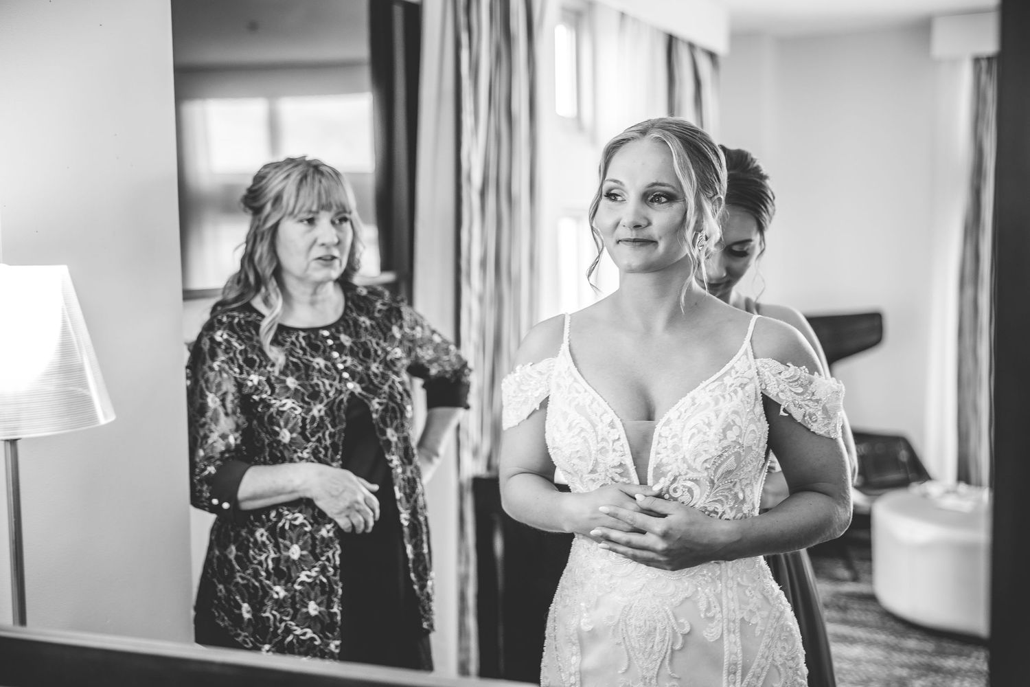 Candid moment of bridal preparation with women helping in a bright room.