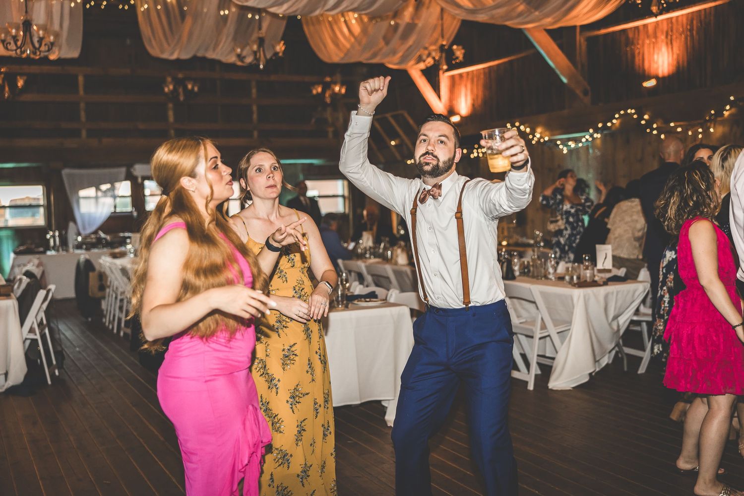Energetic dance party at rustic barn wedding reception with festive lighting.
