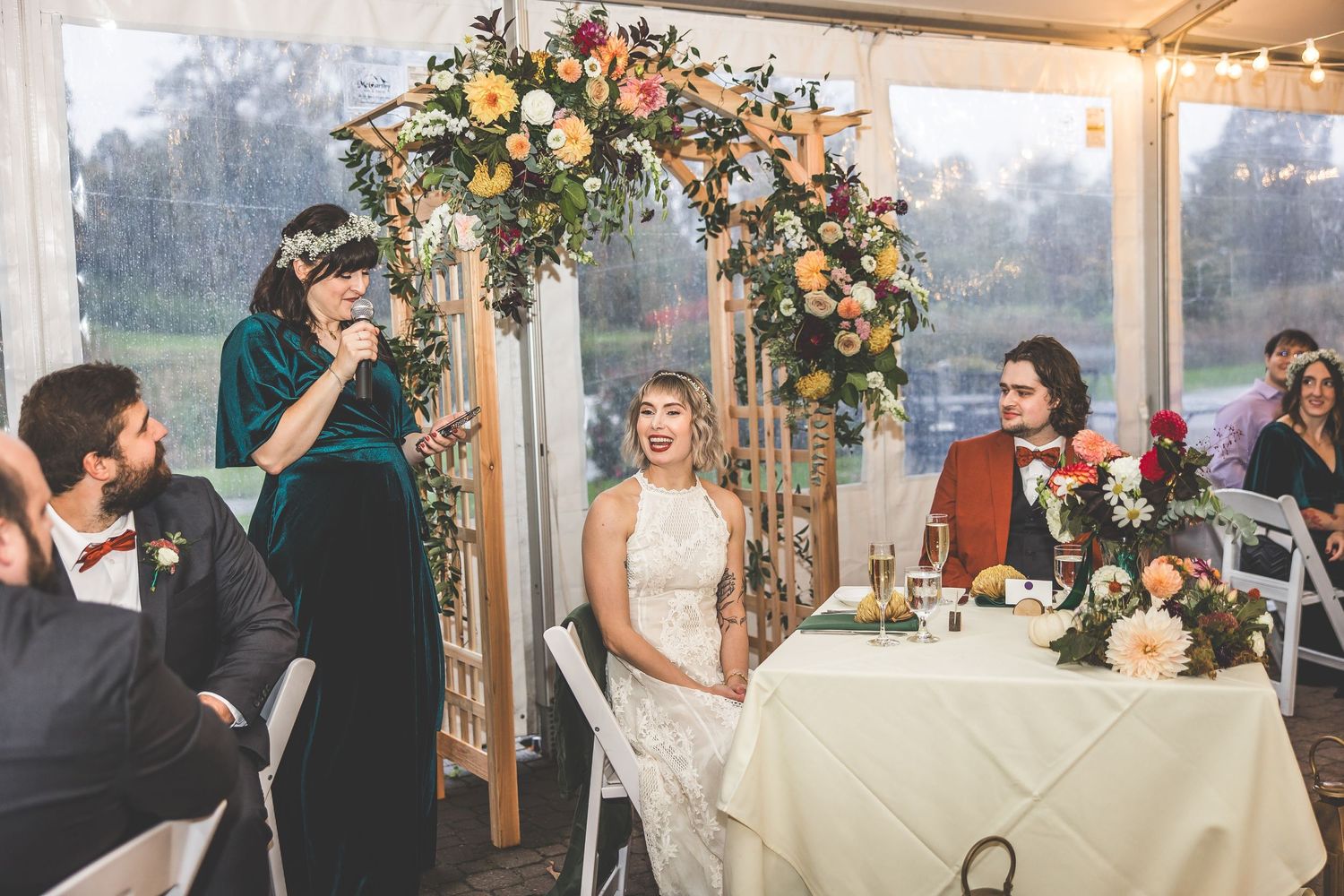 Wedding ceremony setup with floral arch and white chairs under a clear-sided tent.