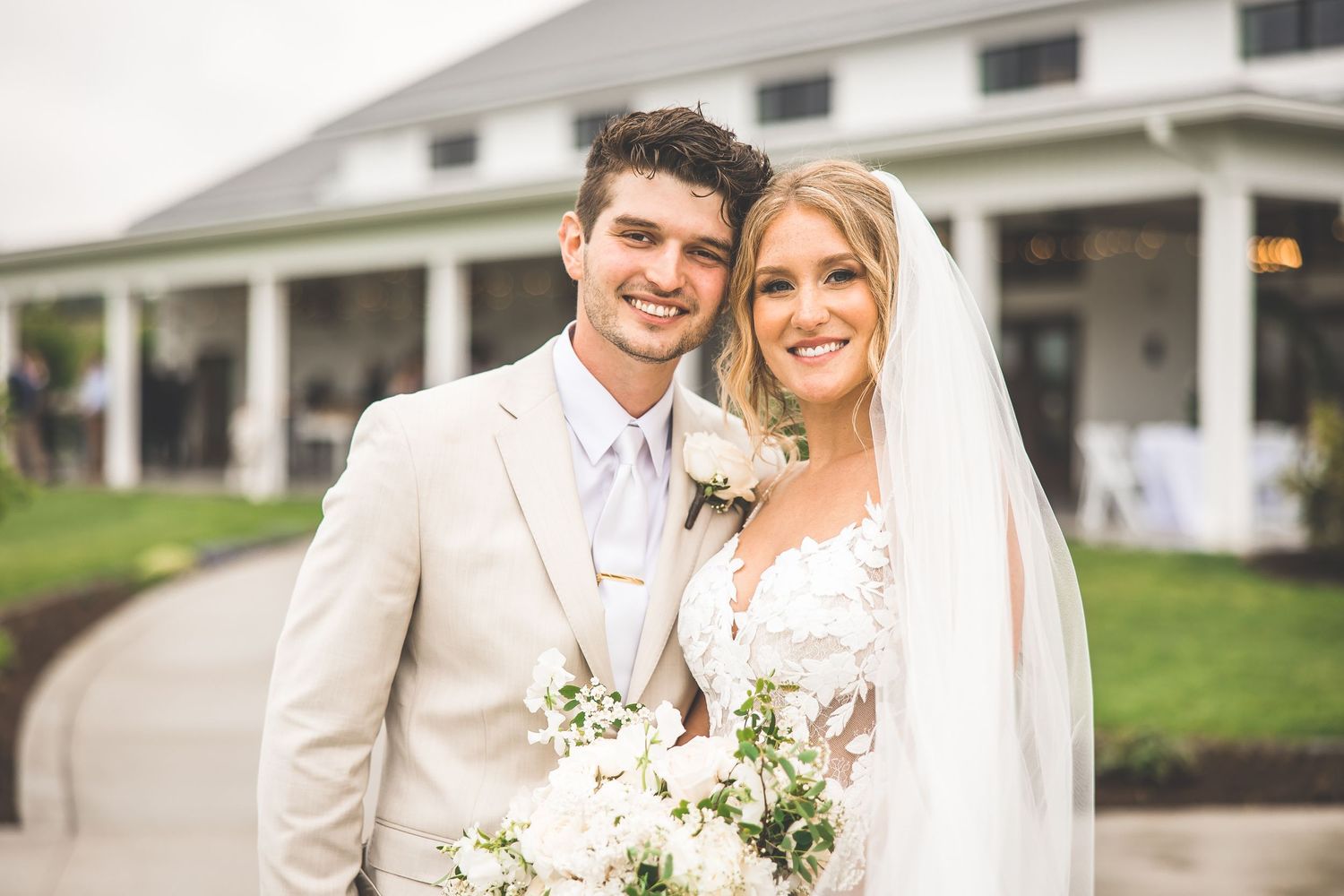 Newlyweds pose together in front of white columned wedding venue.