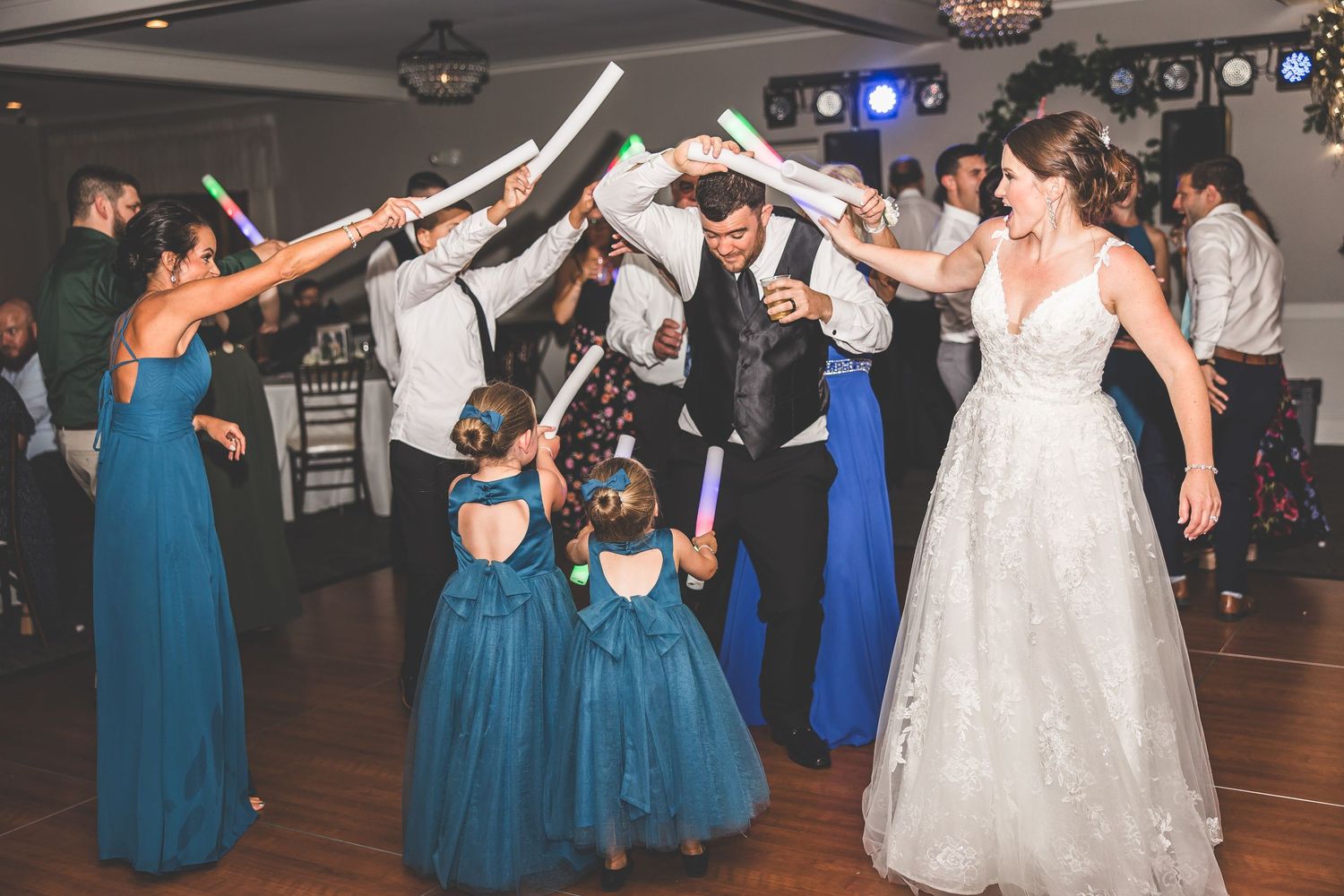 Wedding party dancing at reception with bridesmaids in blue dresses and bride in white gown.
