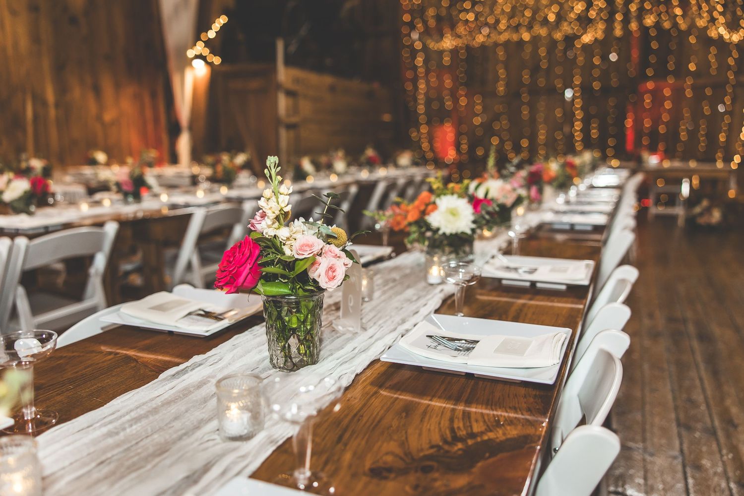 Rustic barn wedding reception tables set with white linens and simple floral centerpieces.