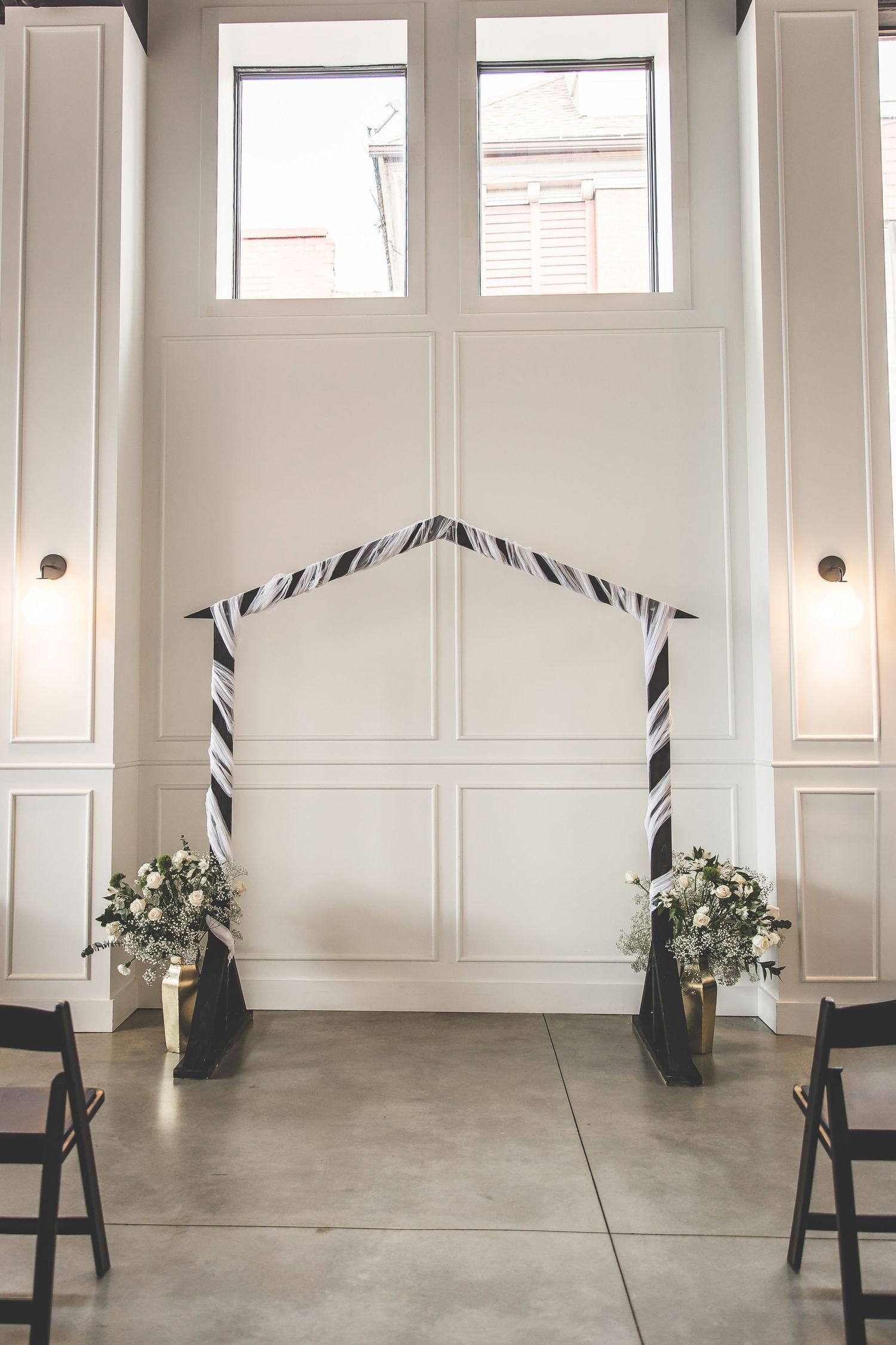 Minimalist white event space with tall windows and decorative wall paneling.