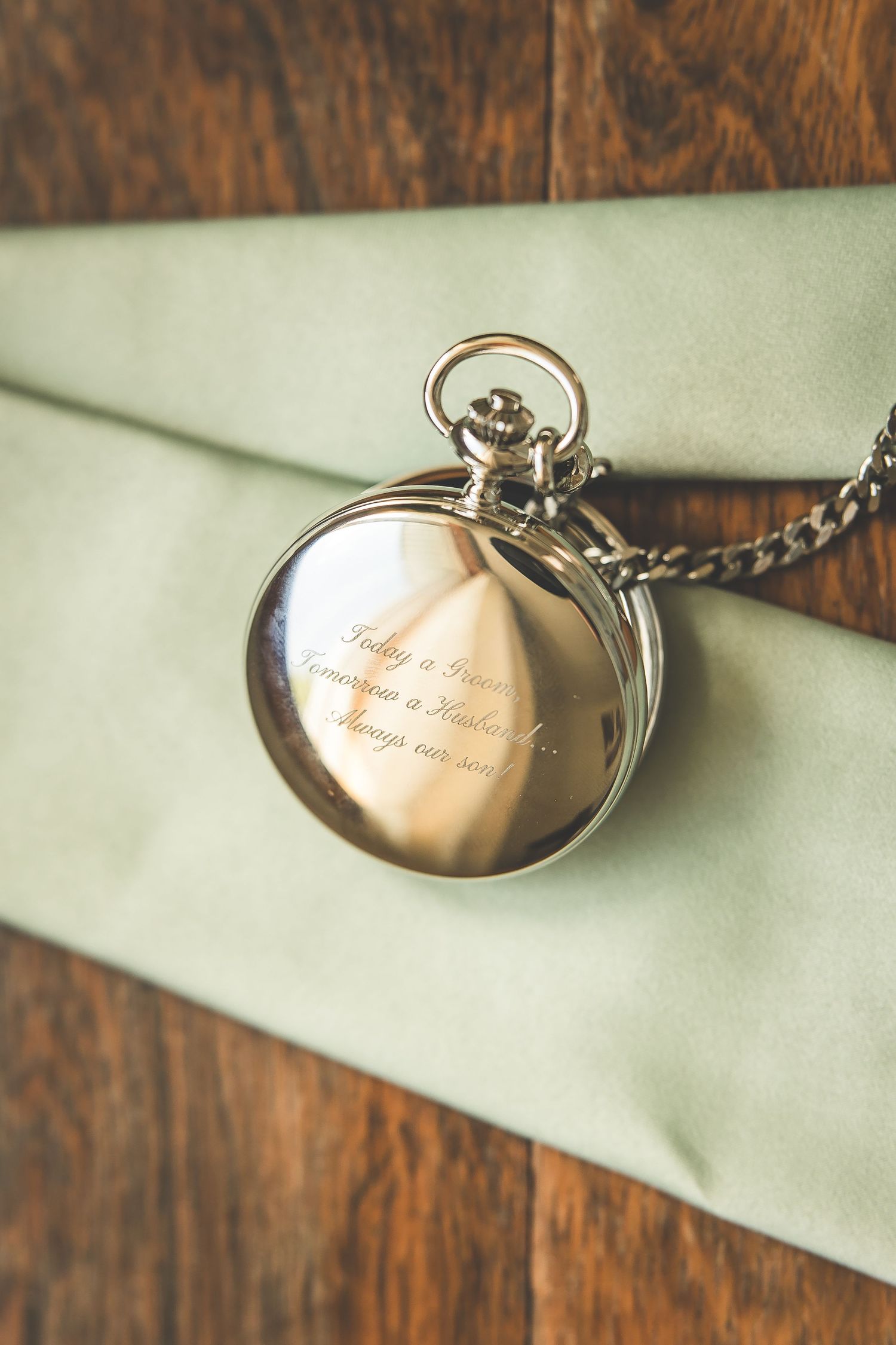 Vintage pocket watch on sage green fabric displays engraved details.