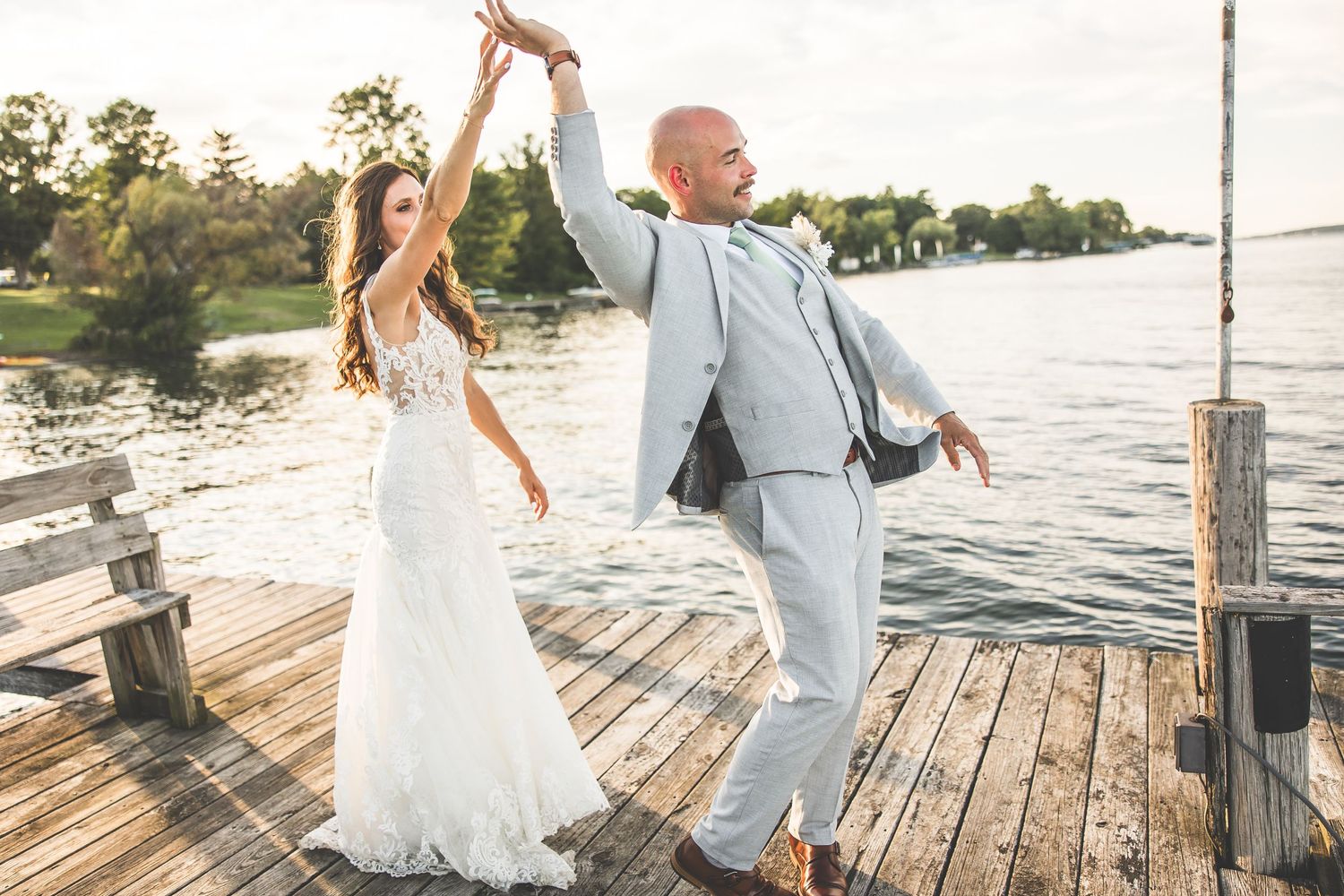 Dancing and twirling wedding couple on wooden dock by the lake.