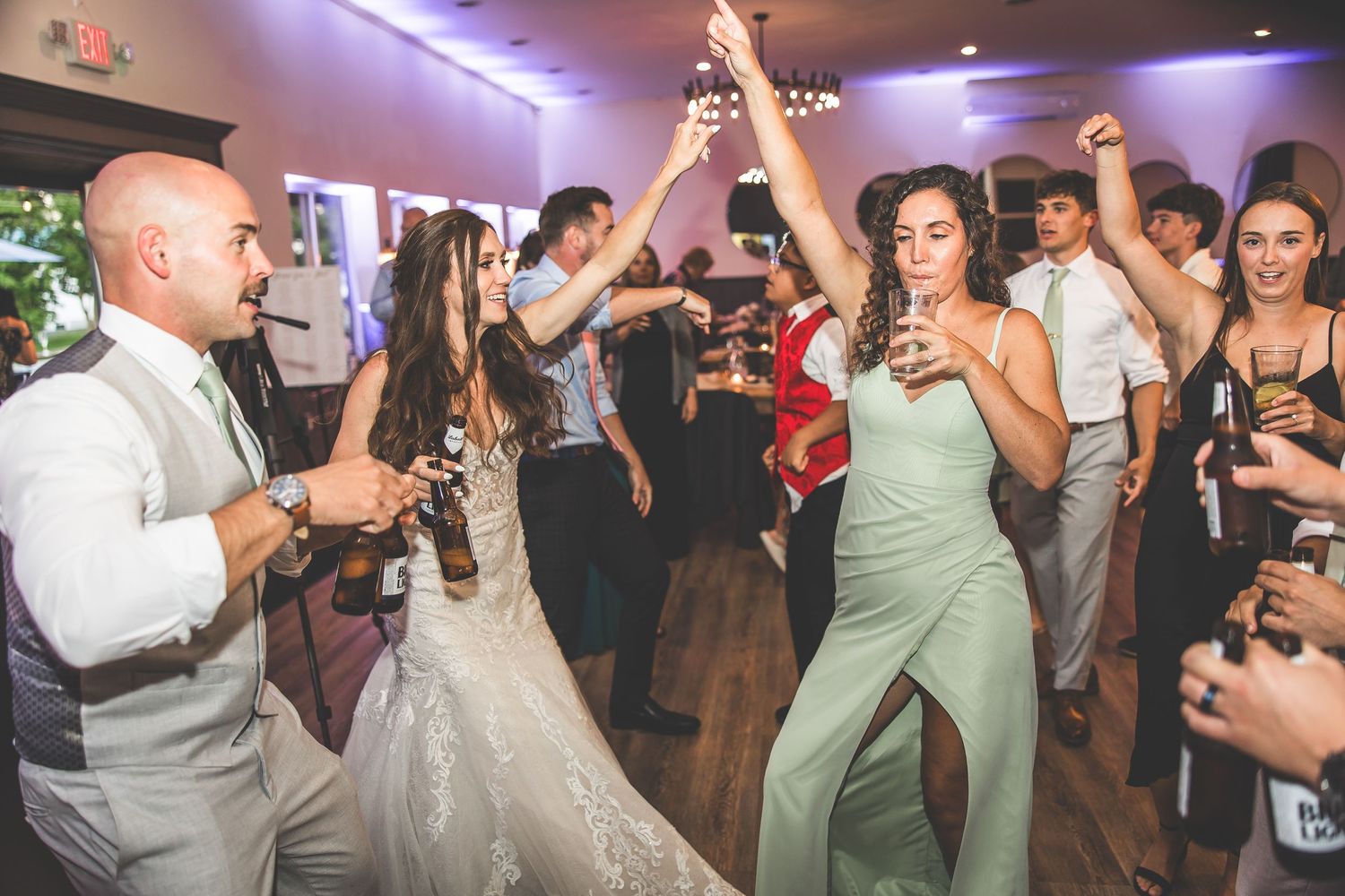 Wedding guests dancing and celebrating under purple reception lighting.