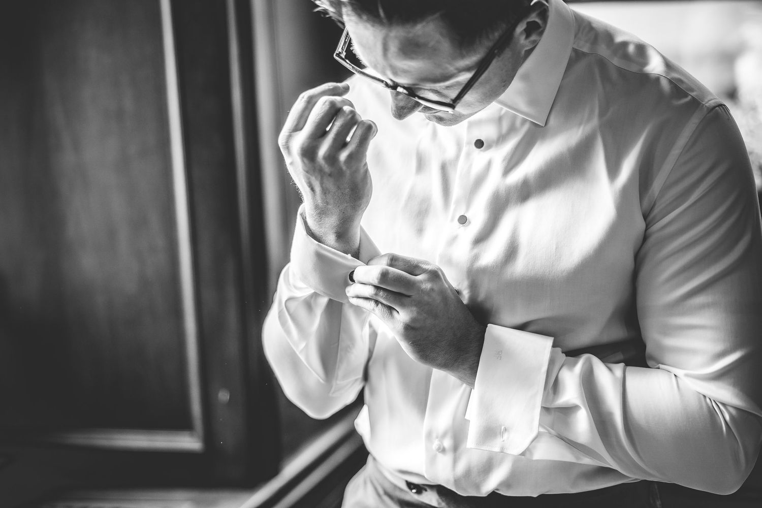 Close-up of person adjusting white dress shirt cuffs near window.