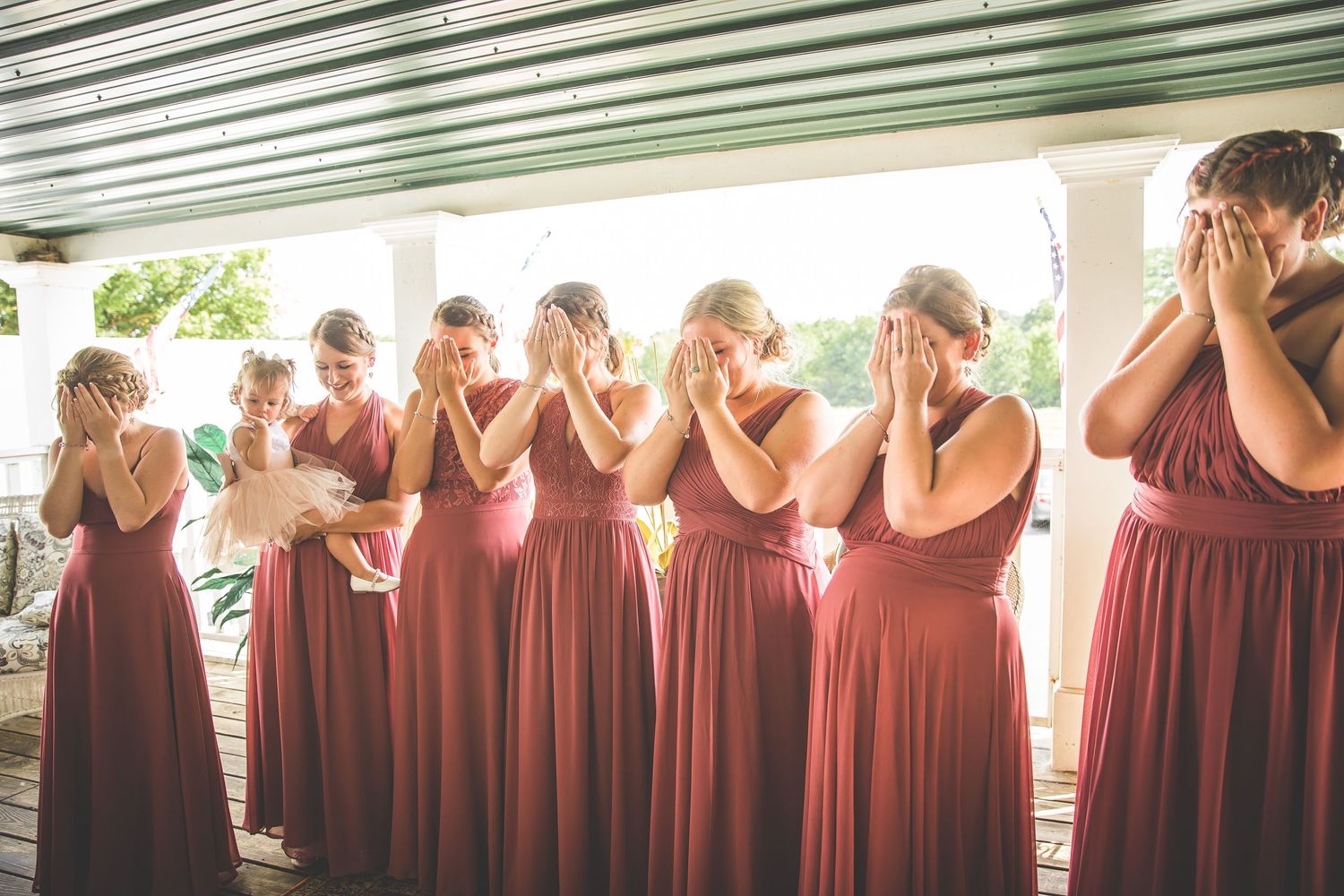 Row of bridesmaids in burgundy dresses standing together at a wedding venue.
