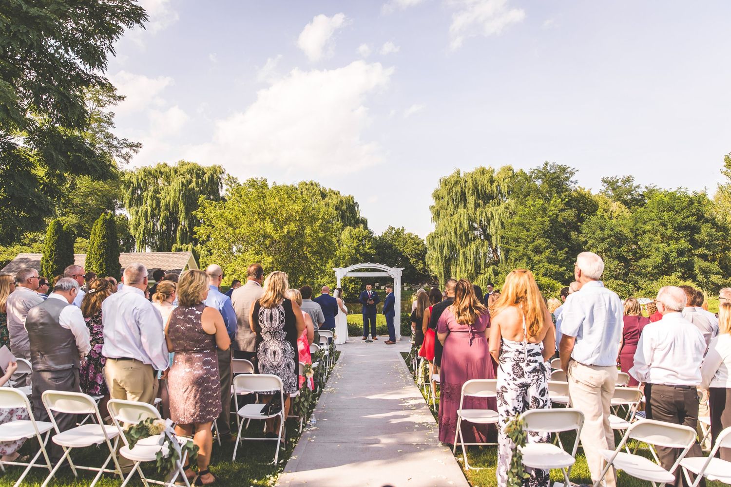 Rows of white chairs set up for an outdoor wedding ceremony with natural landscaping.