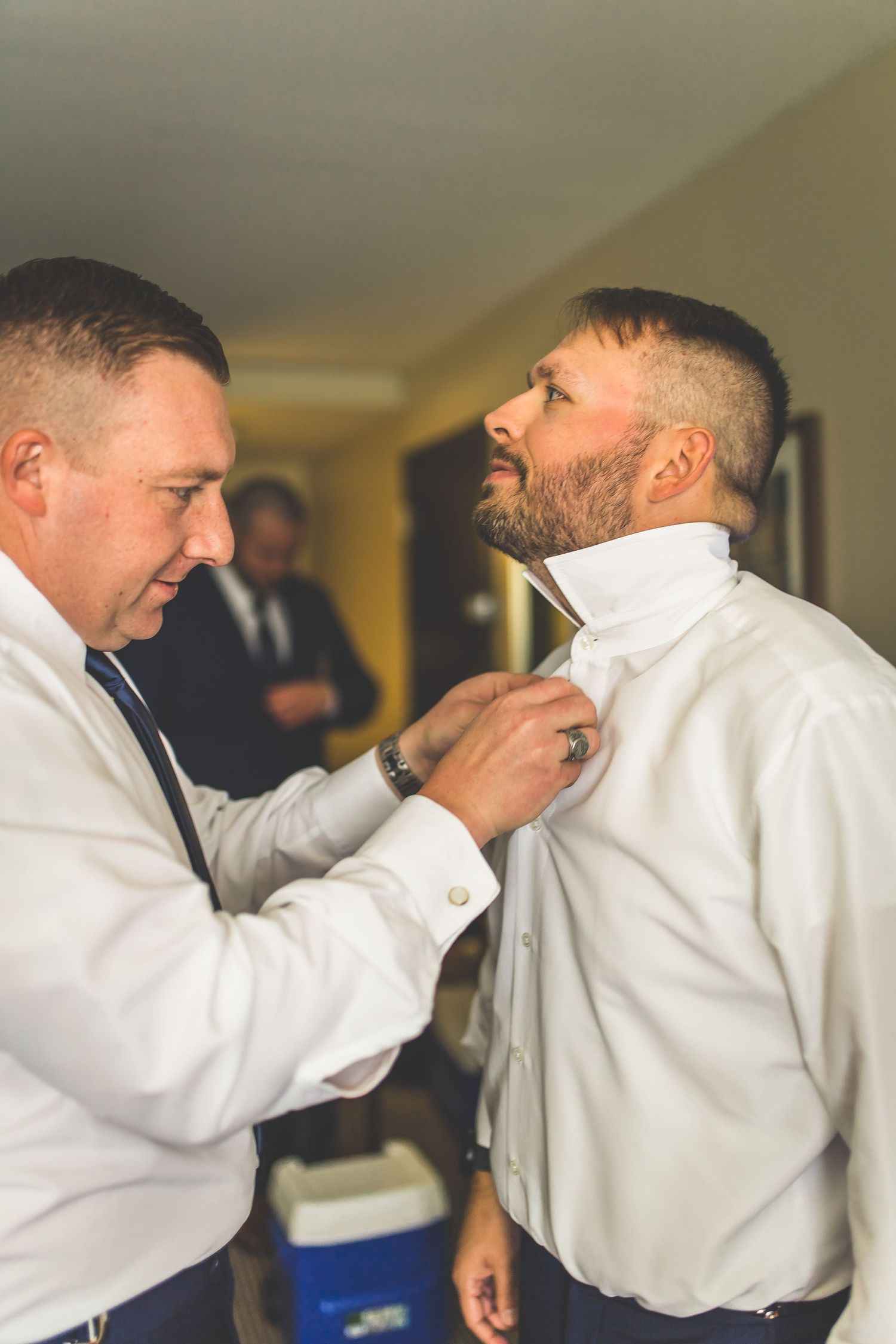 Men in white dress shirts helping each other prepare formal attire before event.