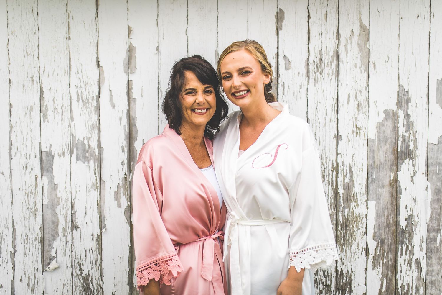 Joyful wedding party in white and pink robes posing together outdoors.