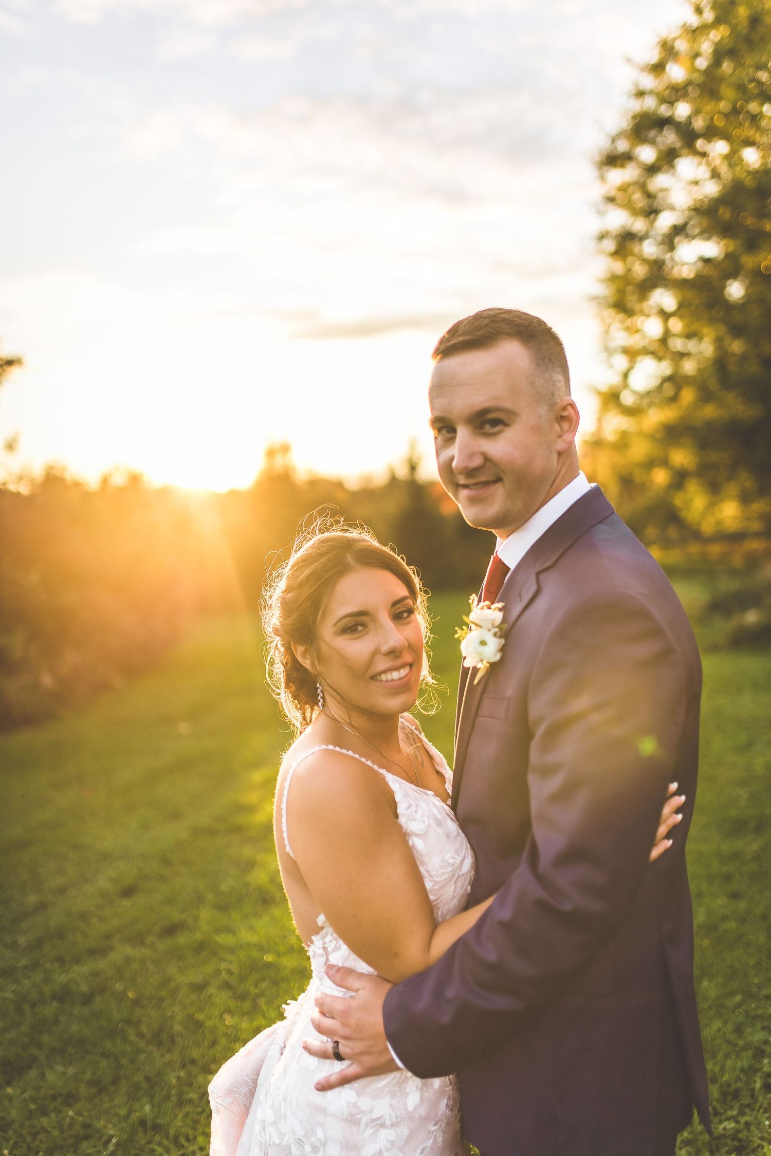 Golden hour portrait of newlyweds embracing in a sunlit meadow.