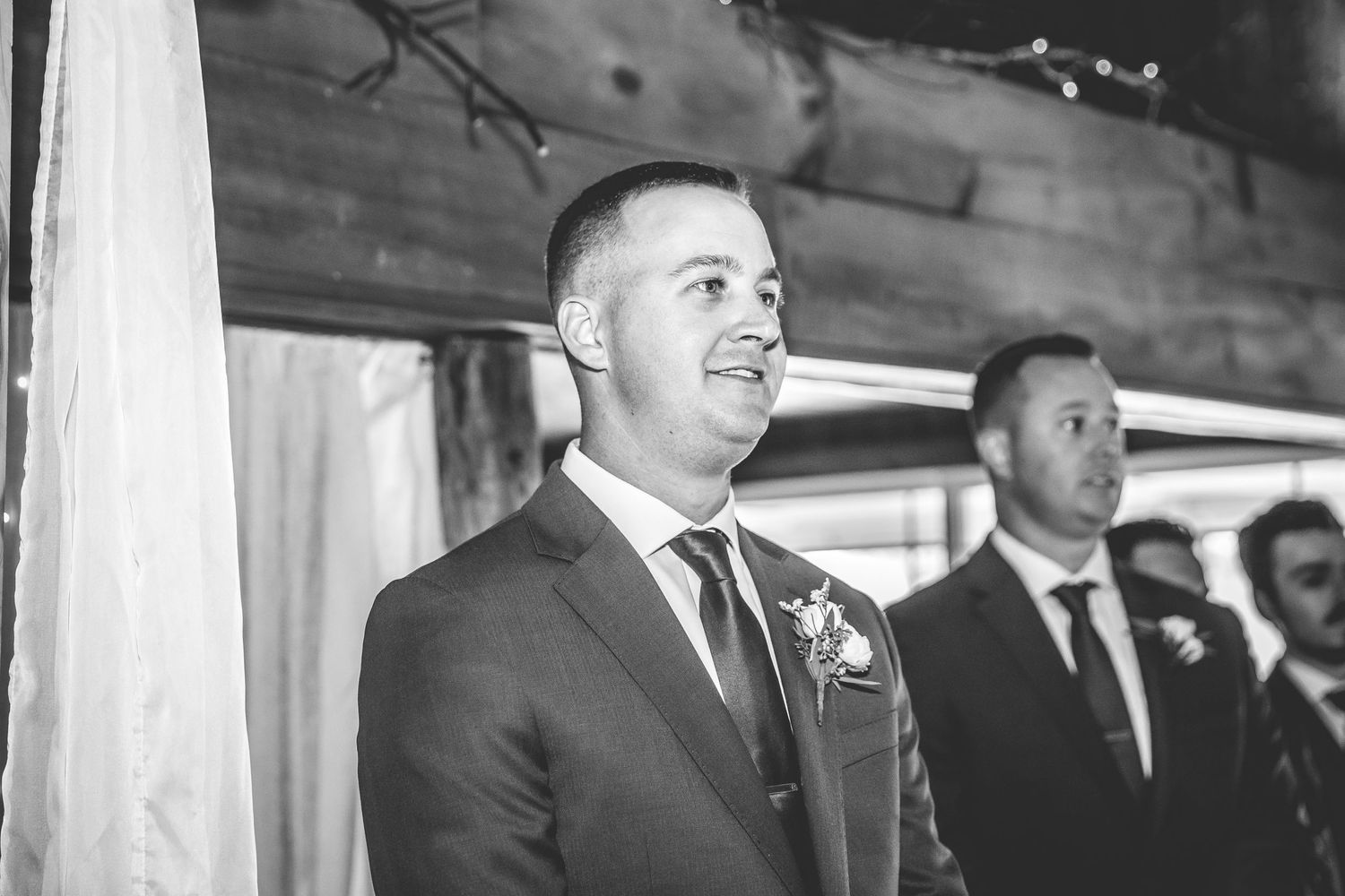 Wedding ceremony guests seated in rustic barn venue with exposed wooden beams.