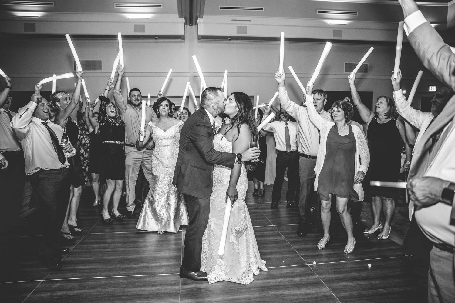 Black and white photo of wedding guests dancing with light-up sticks at a reception party.