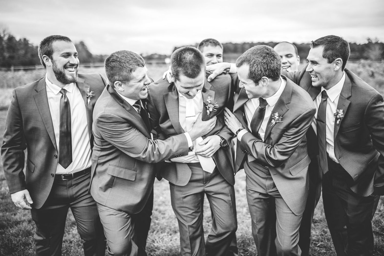 Wedding party members laugh and joke together in a candid group photo.