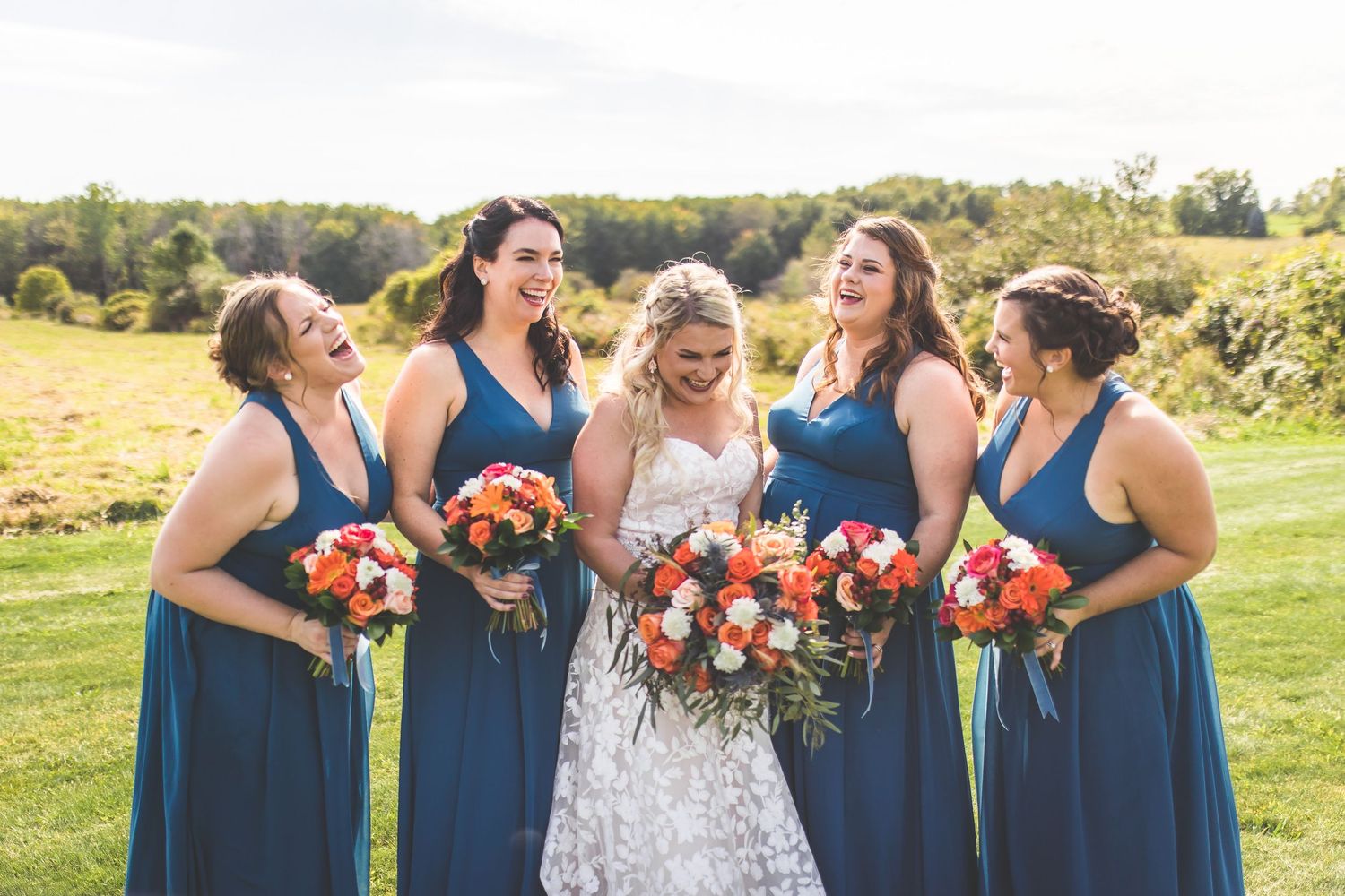 Bridesmaids in navy dresses share joyful moment with bride in lace gown.