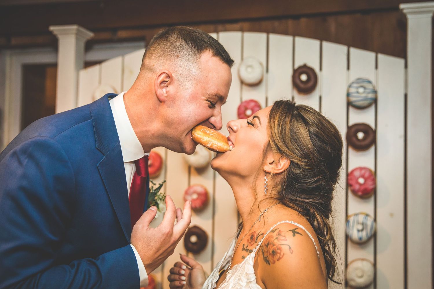 Couple shares playful moments eating donuts during wedding reception in rustic venue.