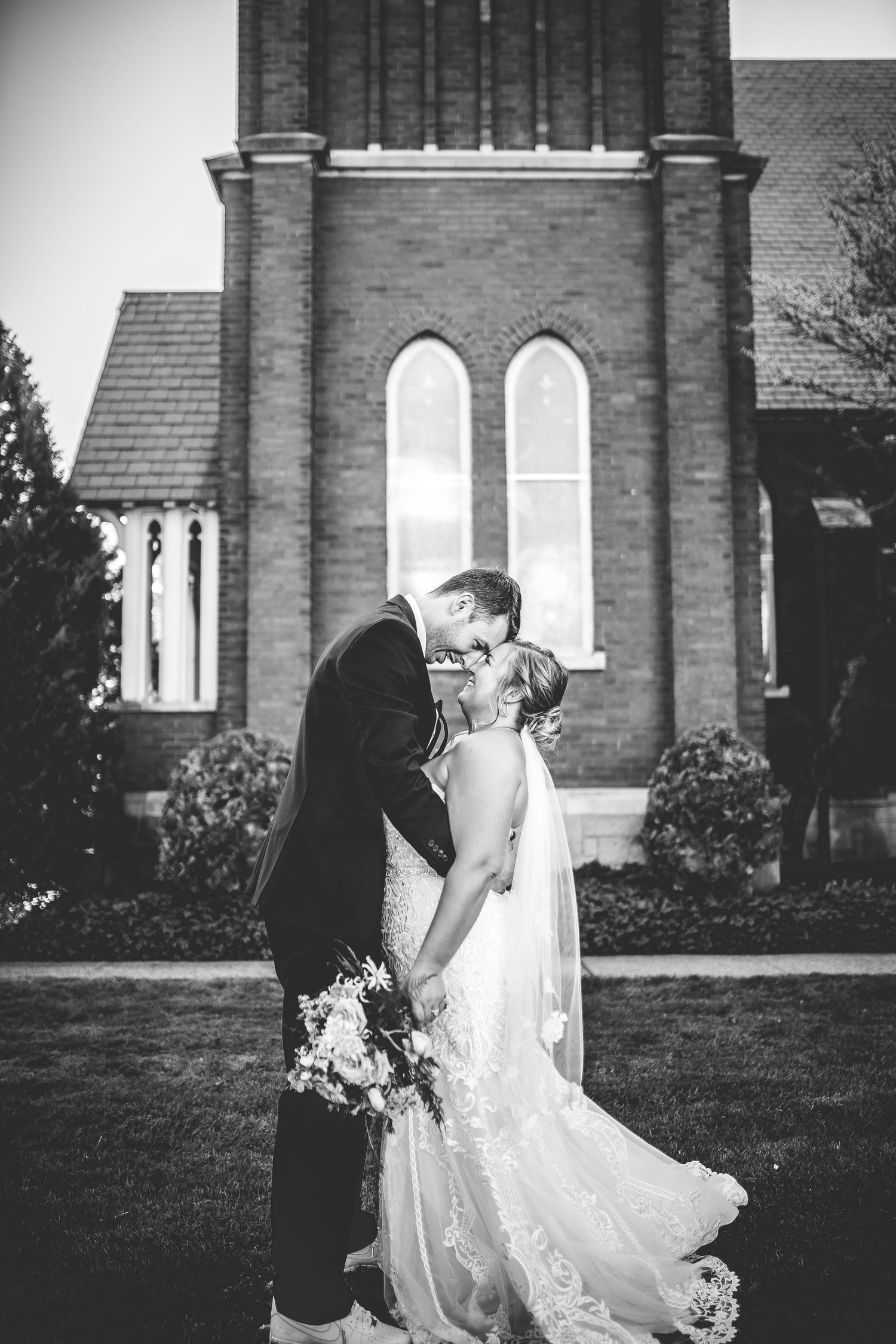 Black and white portrait of wedding couple sharing intimate moment outside historic church.