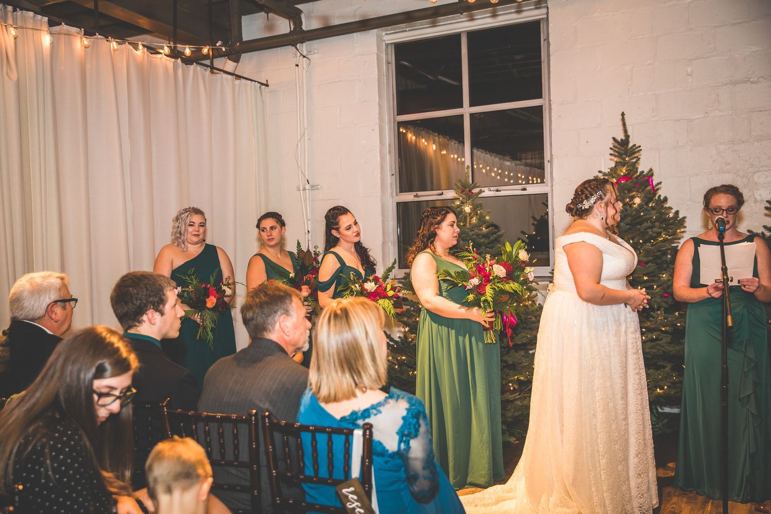 Wedding guests mingle and dance in a festively decorated reception venue with string lights and Christmas trees.