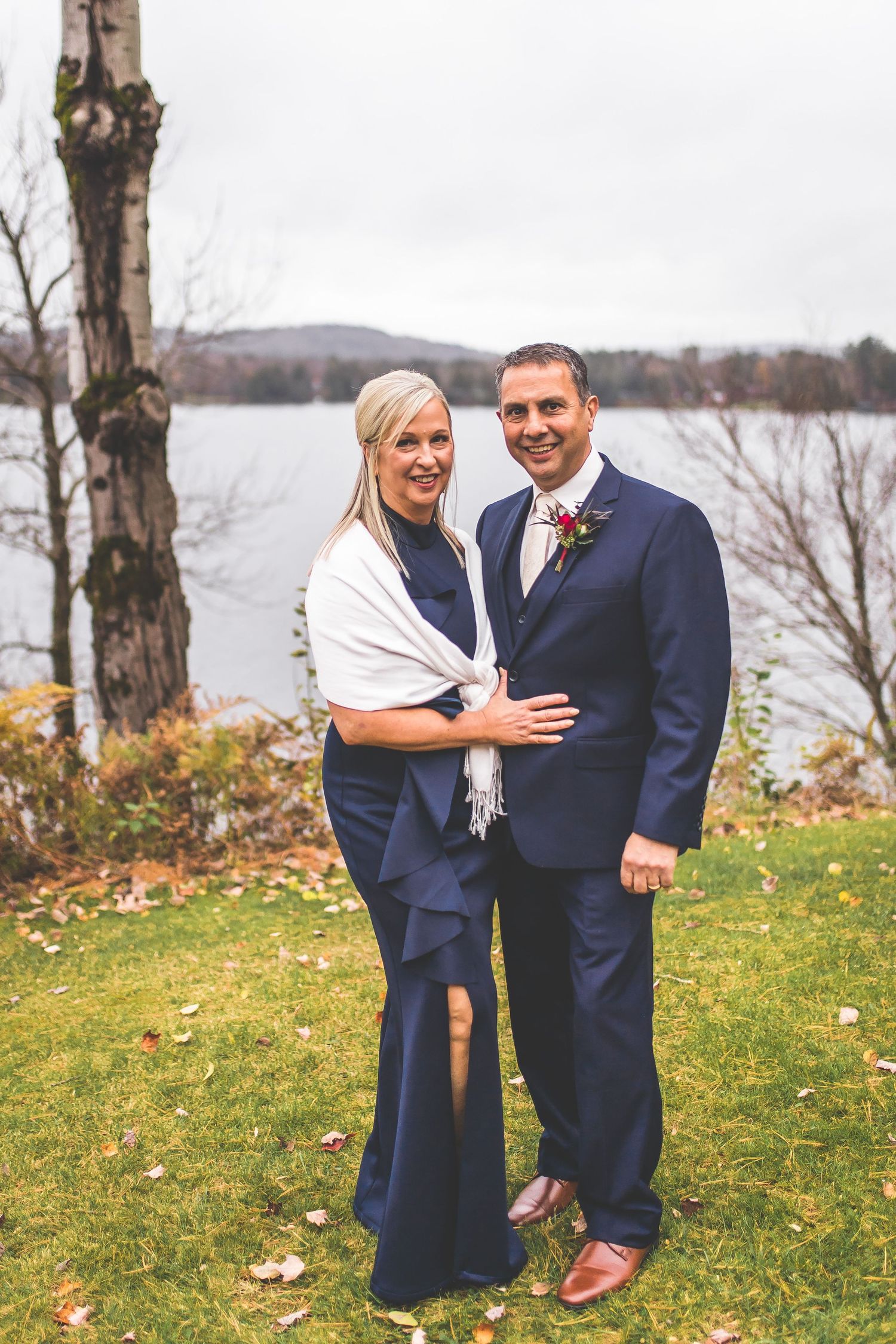 Couple poses together on grassy hillside overlooking water during autumn.