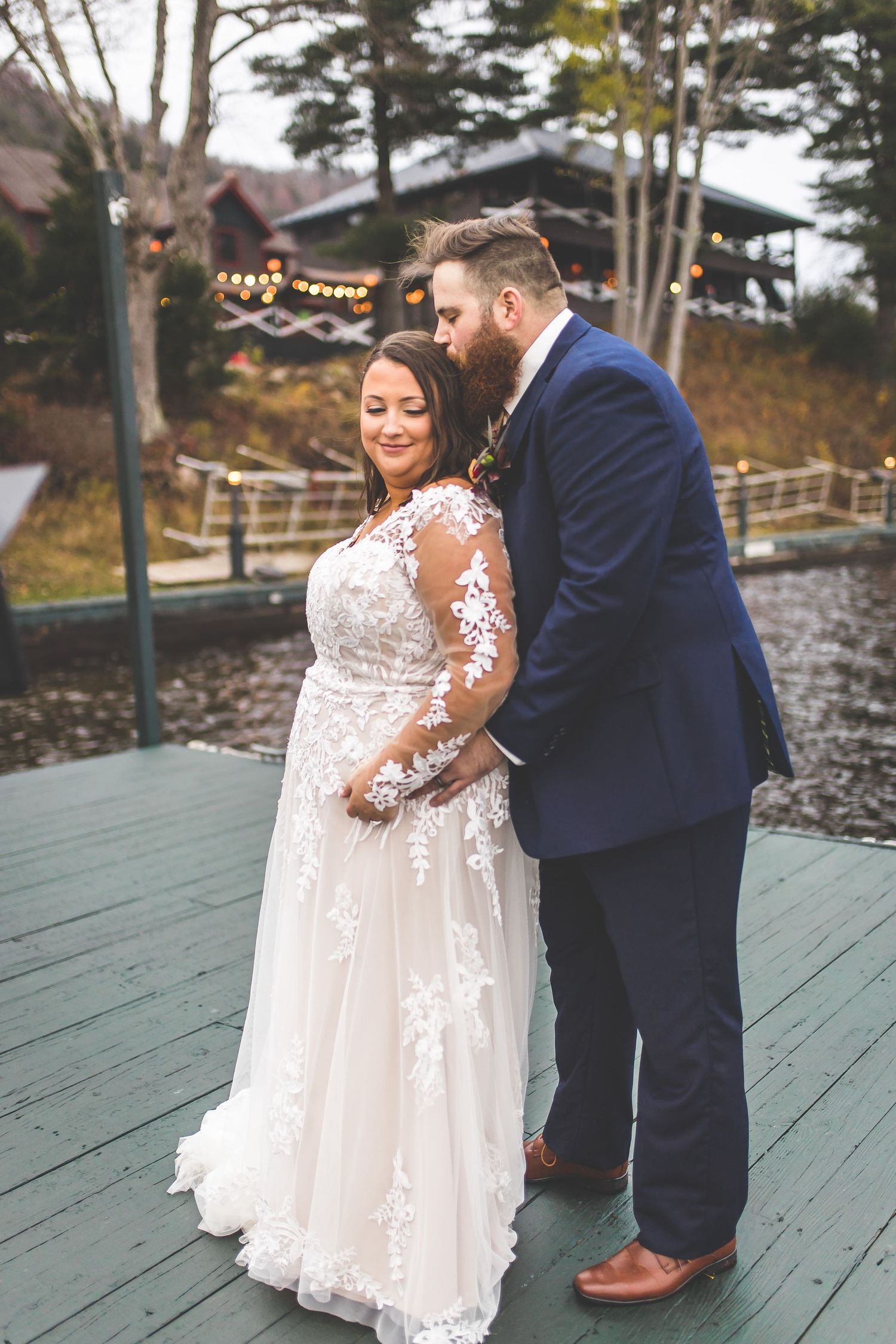 A couple dances together on a wooden deck by the water during their autumn wedding.